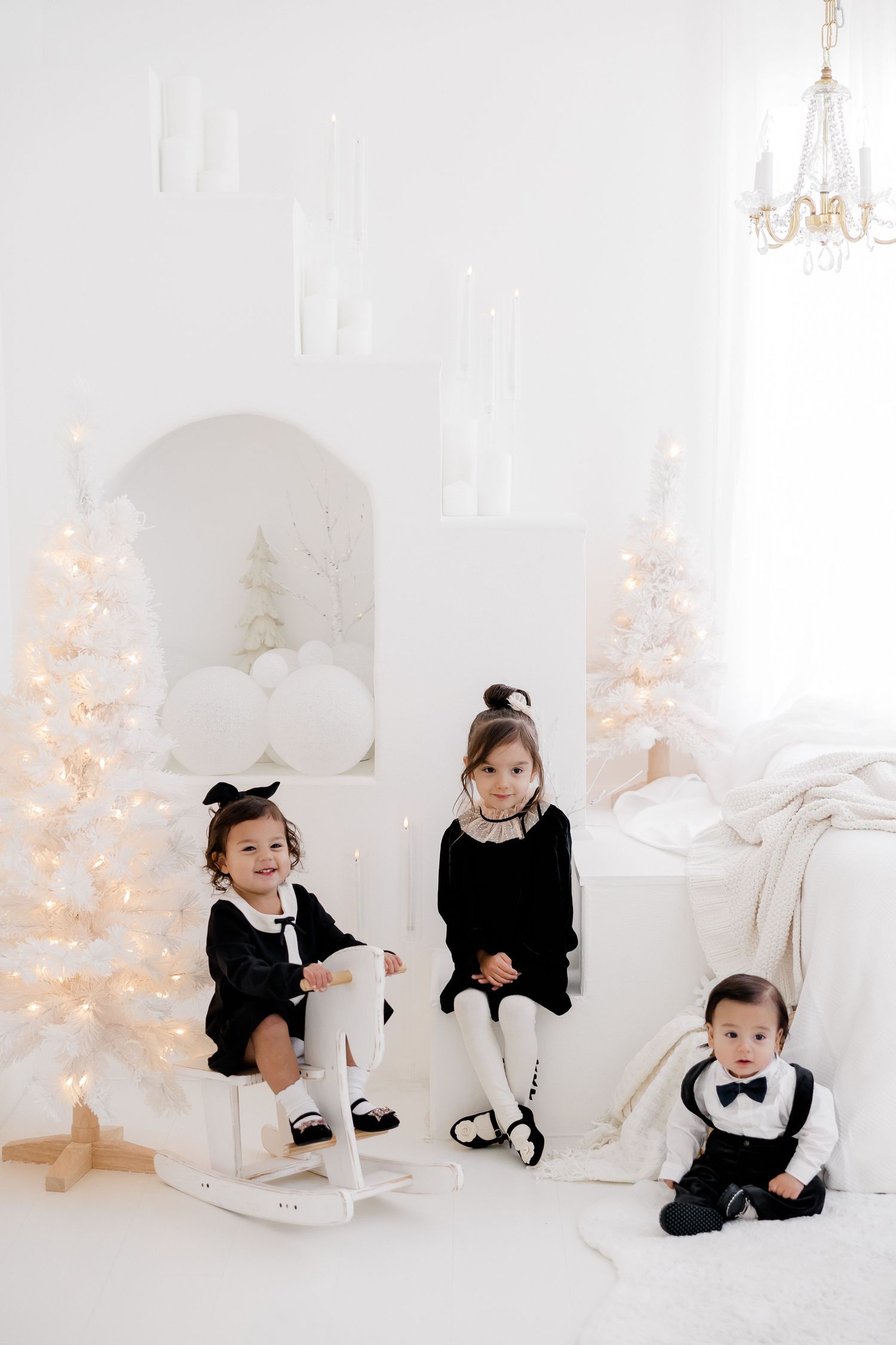 Children in matching black and white outfits pose near white Christmas decorations.