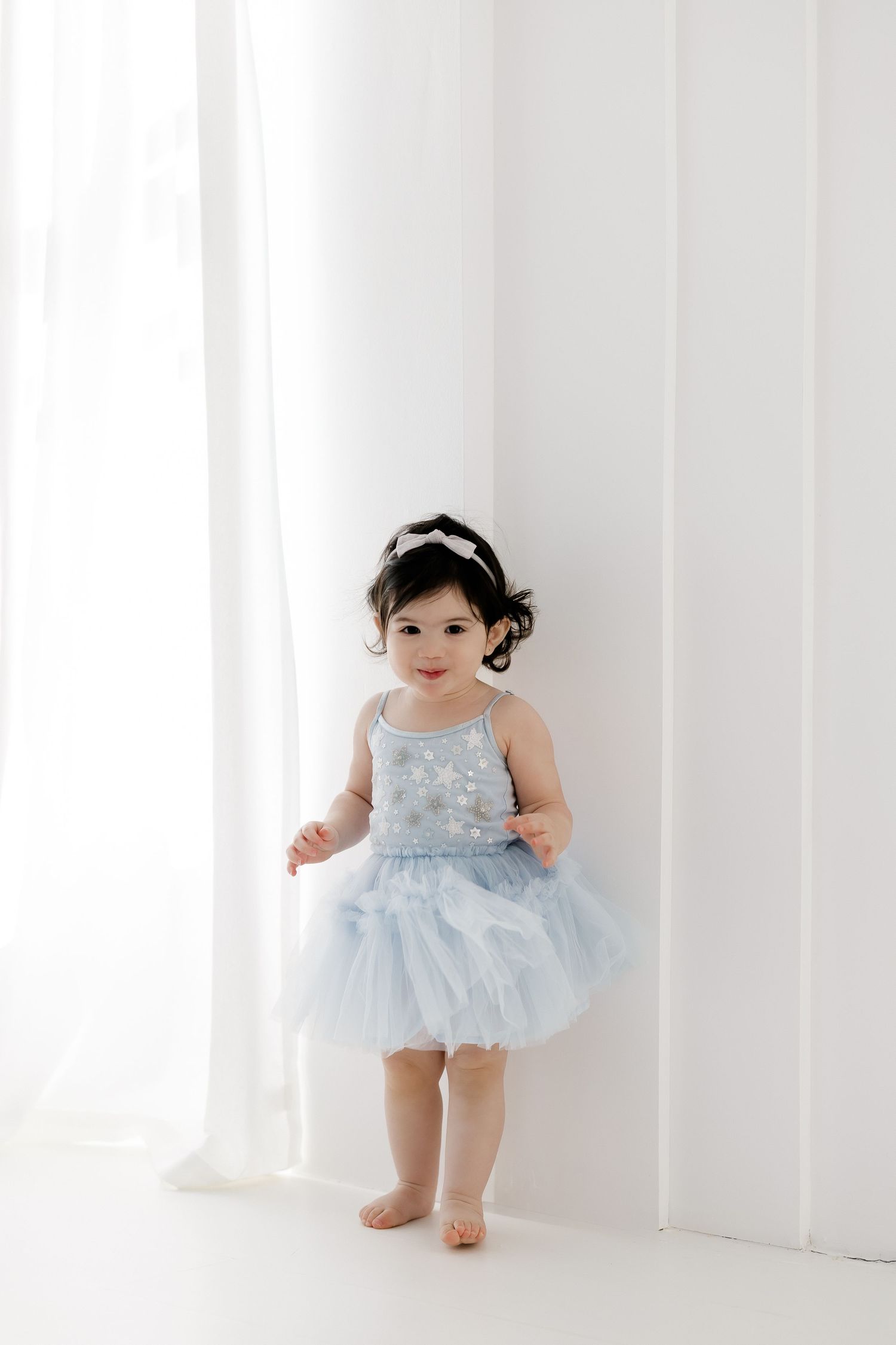 A small child wearing a pale blue tutu dress stands and moves against a white studio backdrop.