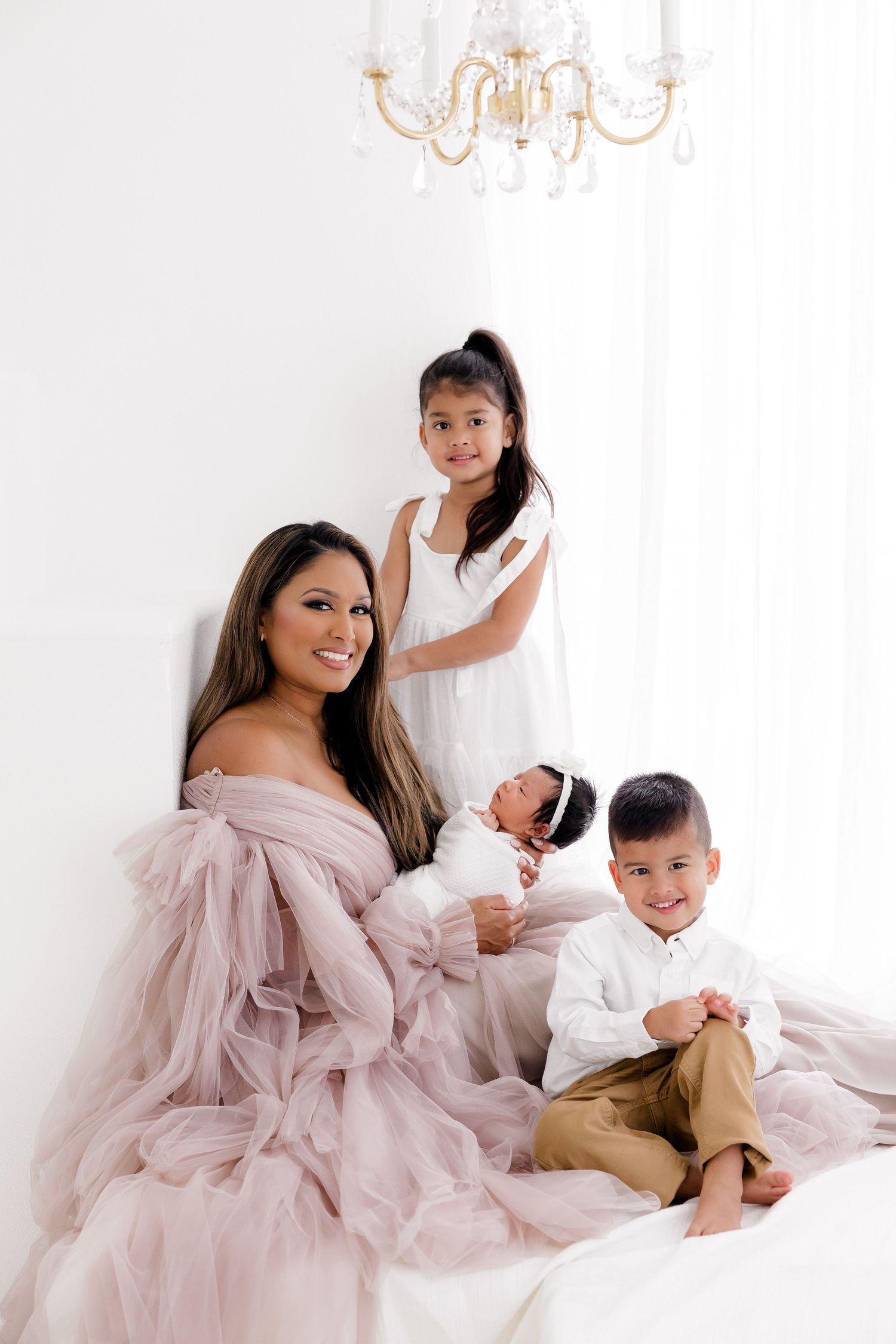 Family portrait with mother in pink gown and children on white bed.