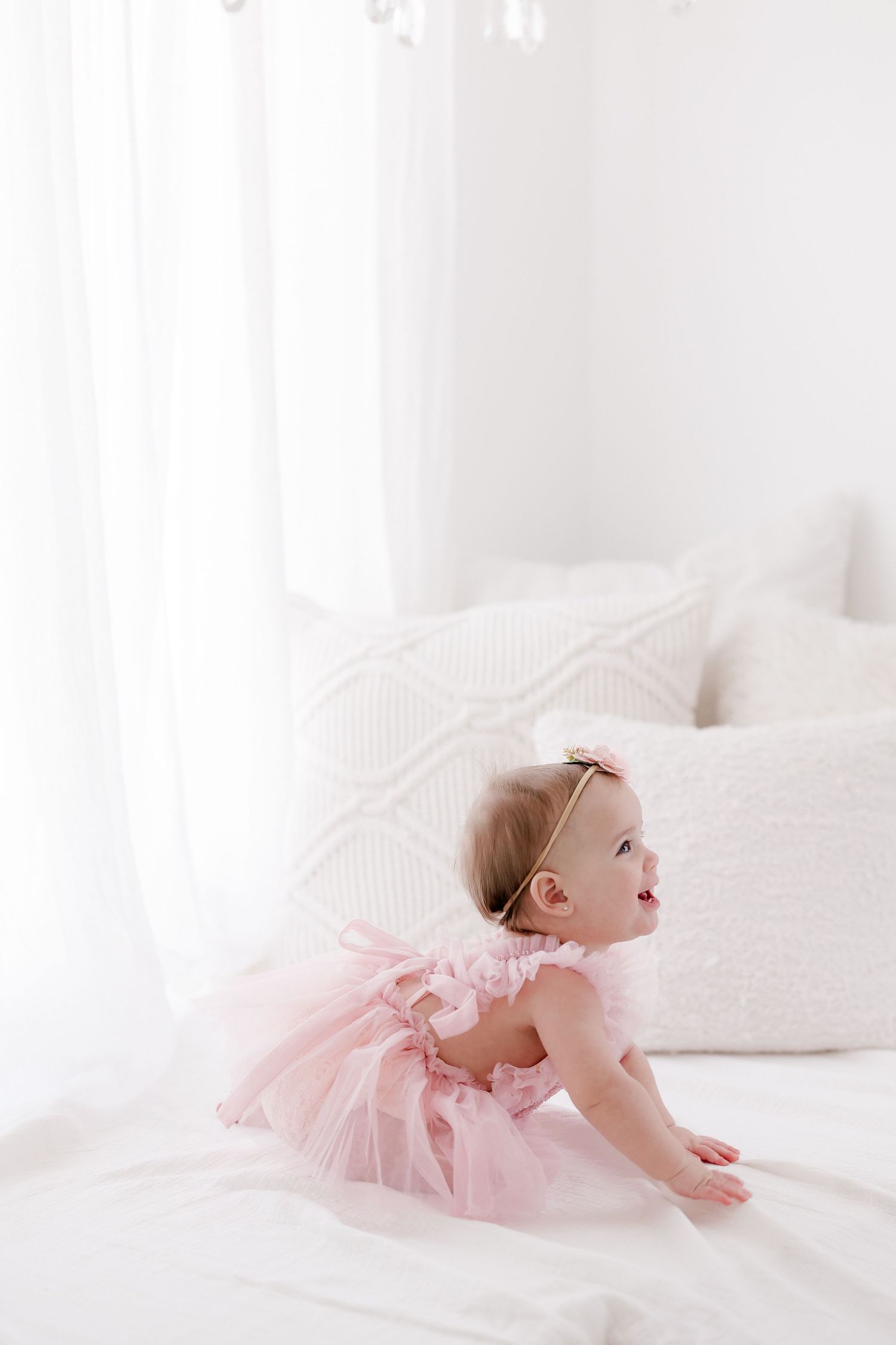 Soft pink tulle dress against white bedding in bright natural light setting.