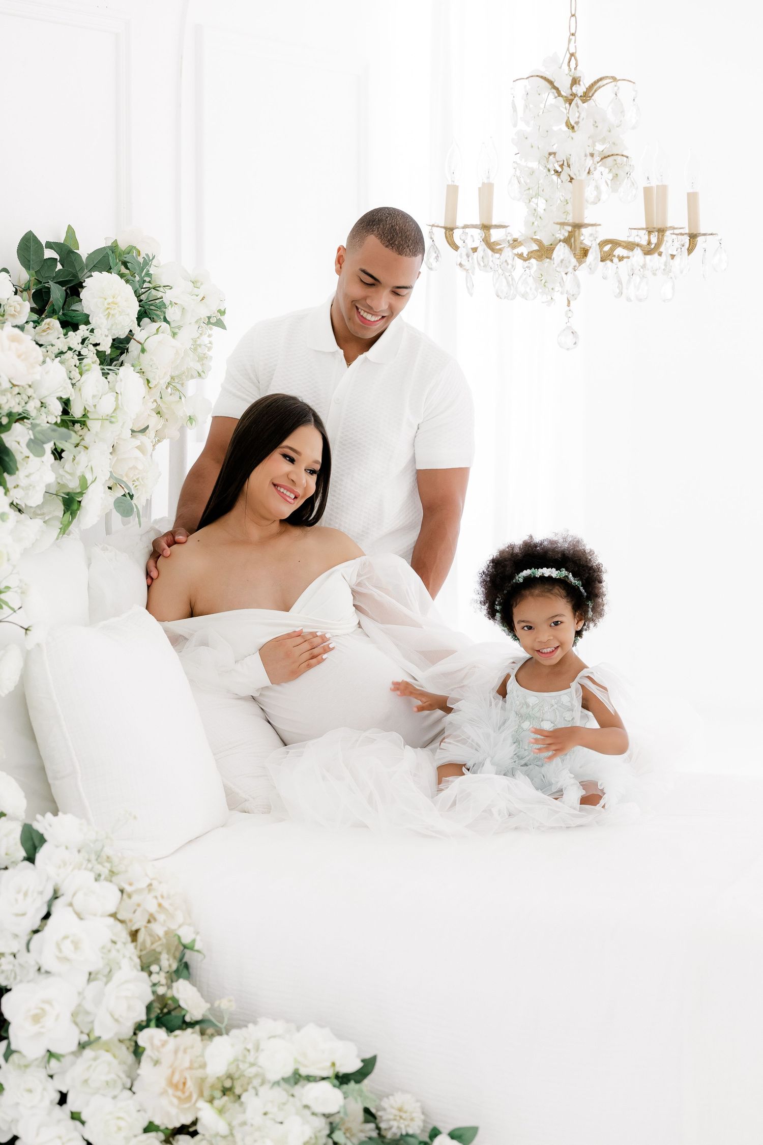 Joyful family maternity session with white decor and chandelier.