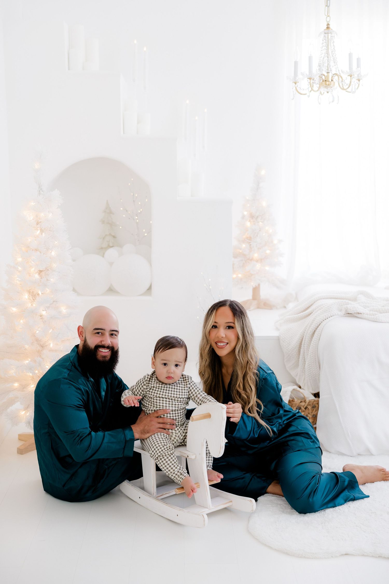 Family relaxes together on white furniture with Christmas decor and soft lighting in background.