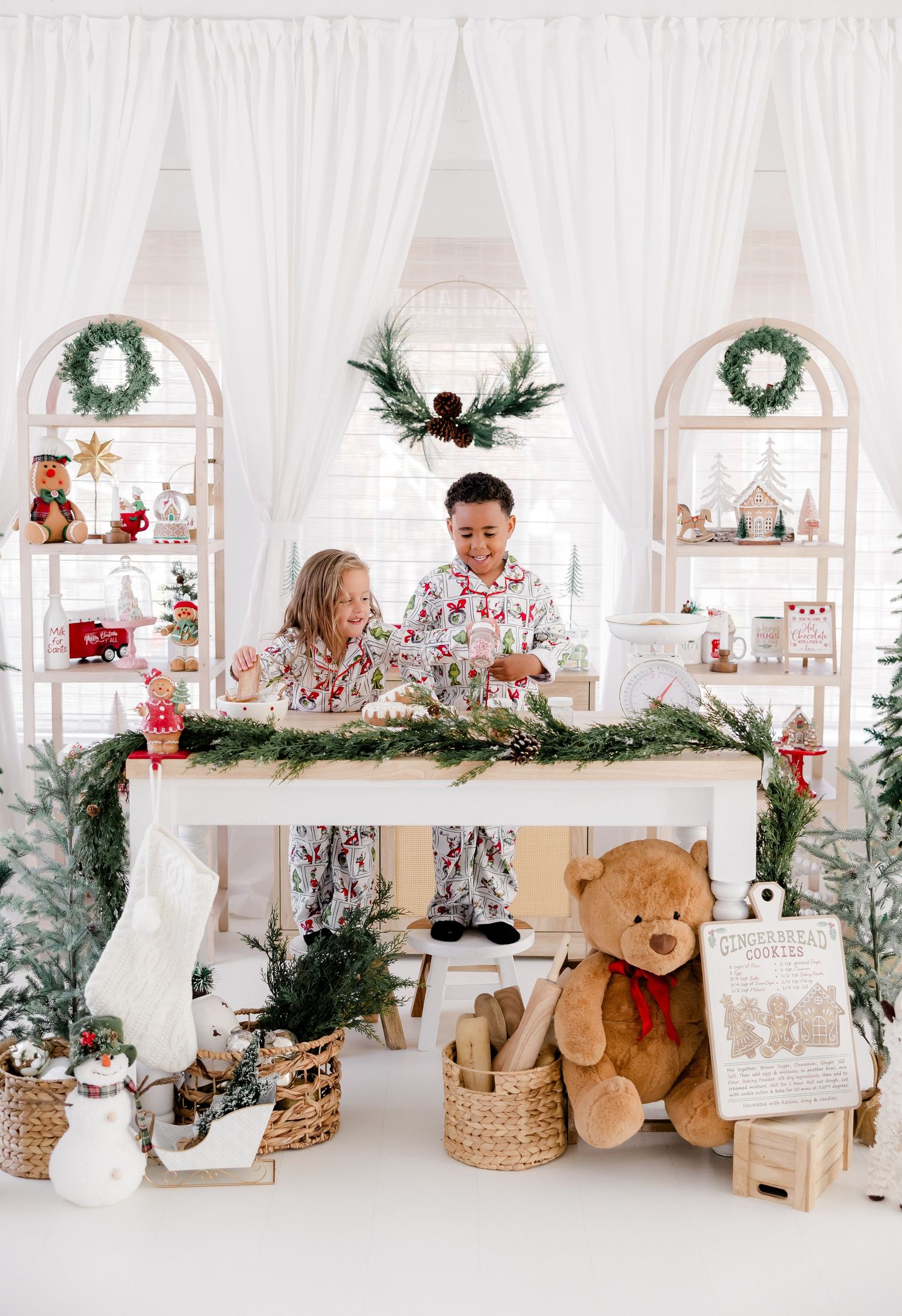 Christmas themed display with white arches, wreaths, and festive holiday decorations in an all-white interior.