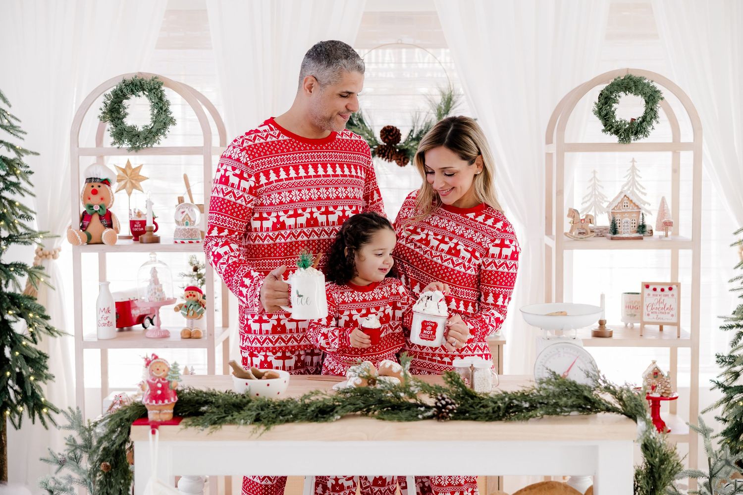 Family wearing matching red Nordic Christmas sweaters gathered around decorated holiday display.