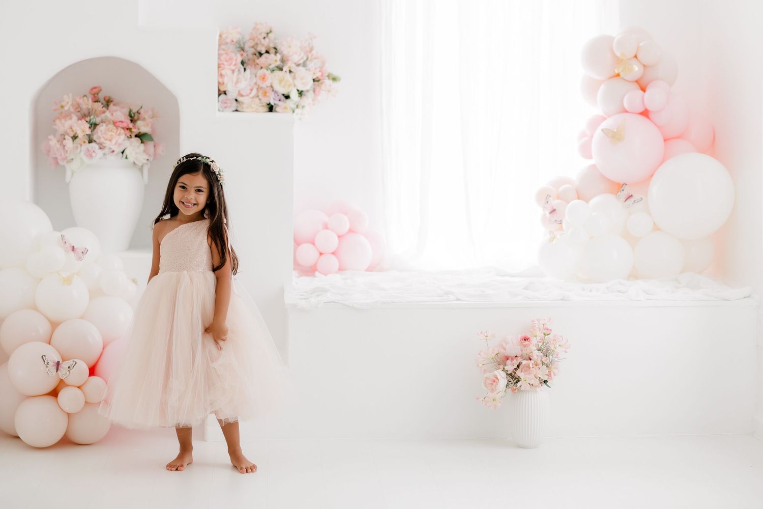 Delicate pink and white balloon garland decorates an elegant all-white studio space for a dreamy photoshoot.