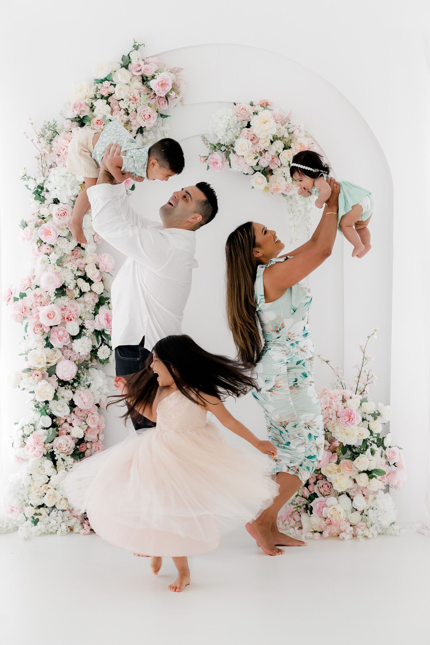 A couple in white and blush pink outfits dance gracefully against a floral backdrop with pink and mint blooms.