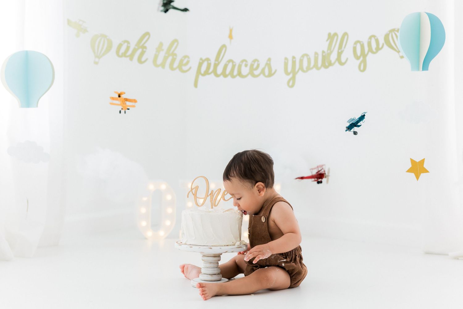 Travel-themed photoshoot with hot air balloon decor and gold lettering on white backdrop.