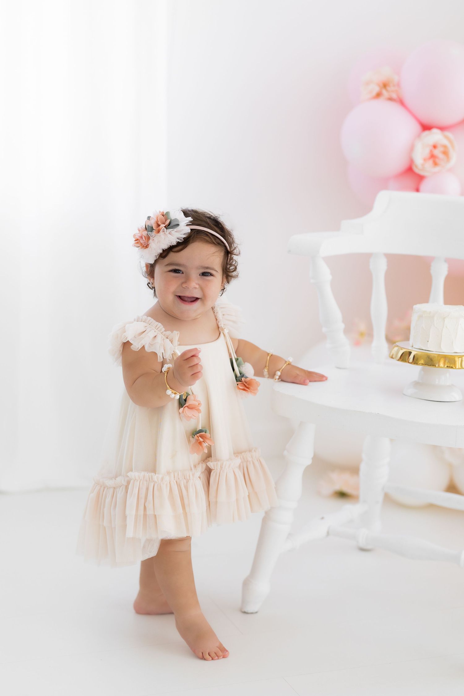 Elegant first birthday photo session with cream dress and floral crown.
