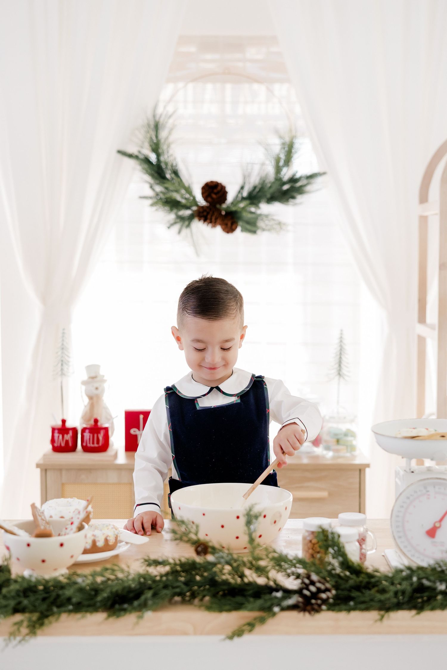 Child in formal attire stirring bowl at holiday-decorated baking station.