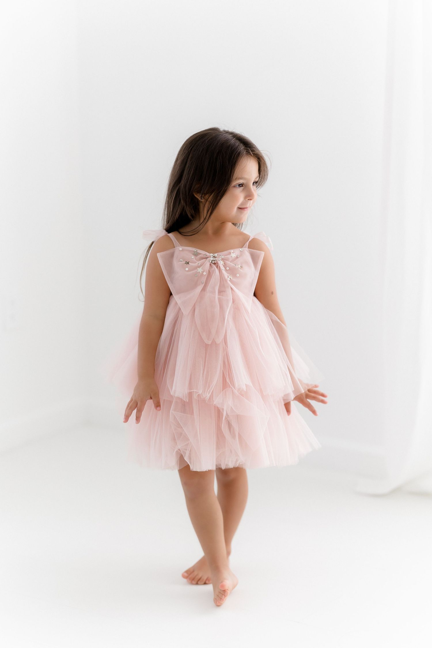 Graceful pink tulle dress captured in minimalist white studio setting.