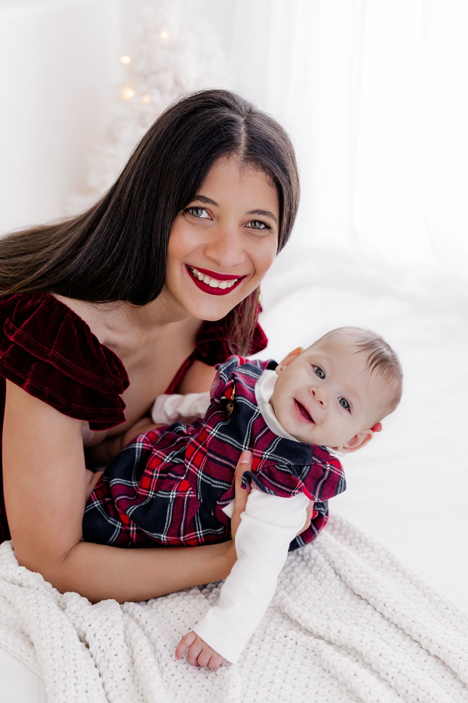 Holiday portrait session on white blanket with plaid clothing and festive Christmas decor.