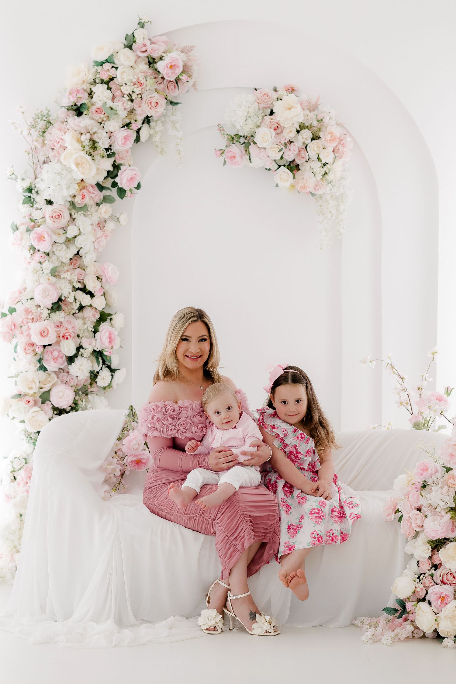 Beautiful floral arch with pink and white roses frames a dreamy portrait setting on white couch with romantic spring decor.