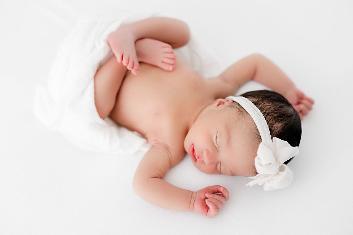 Sleeping newborn with white headband lying on white background in natural pose.