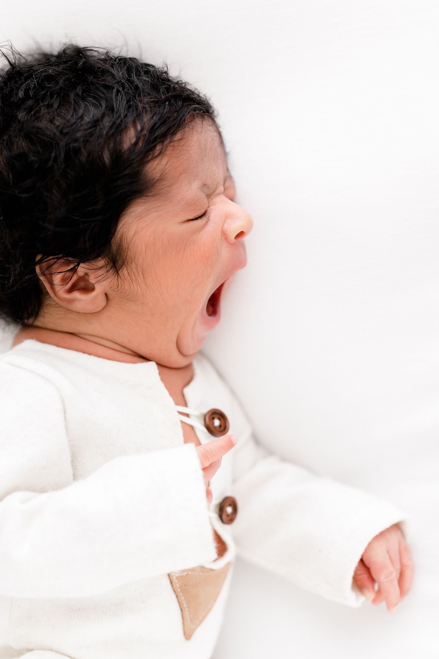 Sleeping newborn in white outfit against white background.