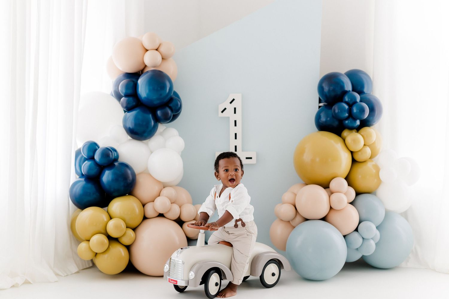 Blue, gold and pastel balloon garland with vintage car decorations creates a whimsical party backdrop.