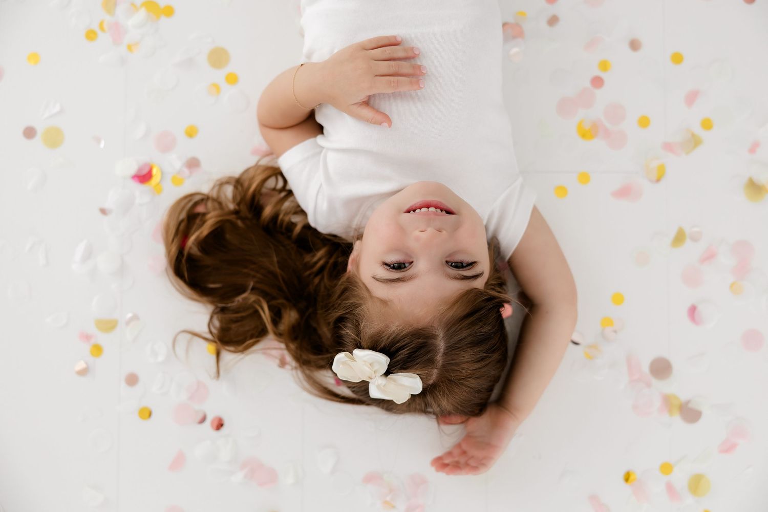 A sleeping baby lies on white fabric surrounded by soft pink and yellow confetti in a composite photo series.