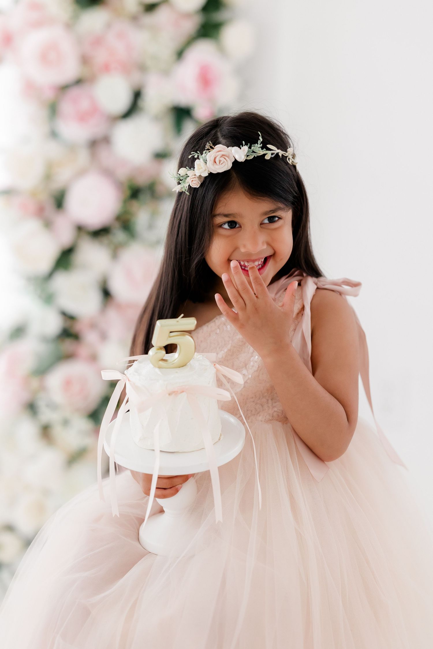 A series of four photos showing a child in a white dress and floral crown against a pink floral backdrop.
