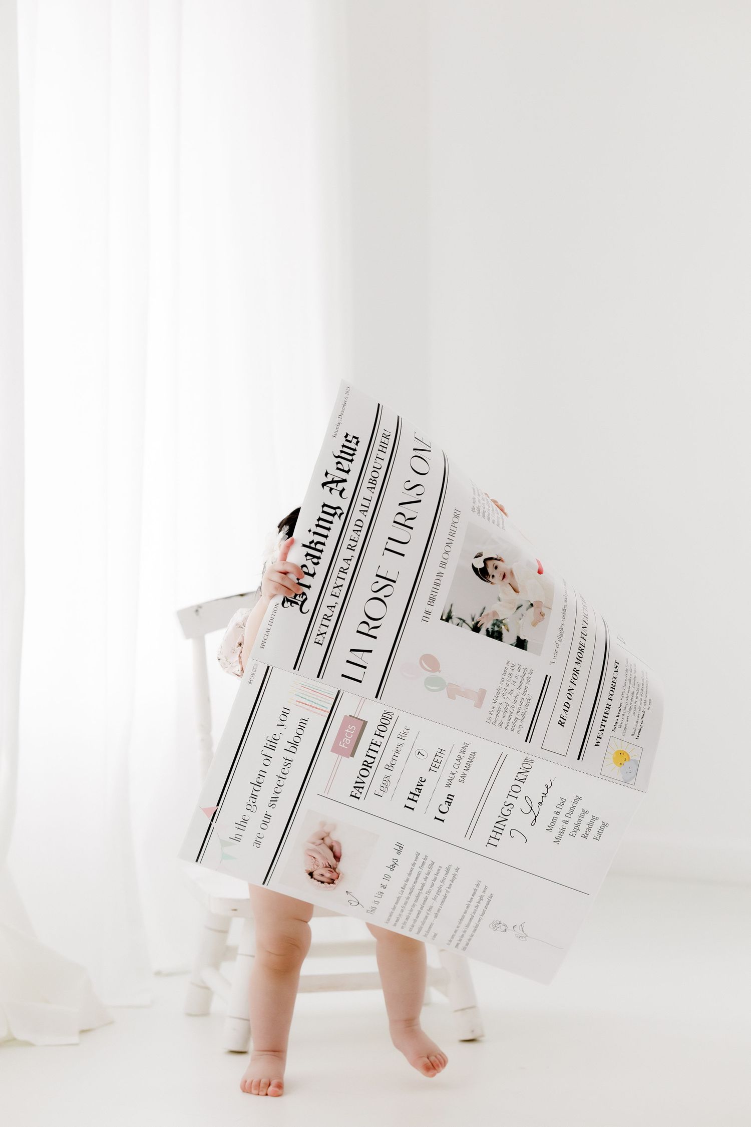 Small bare feet peek out from behind a large newspaper in a minimalist white setting.