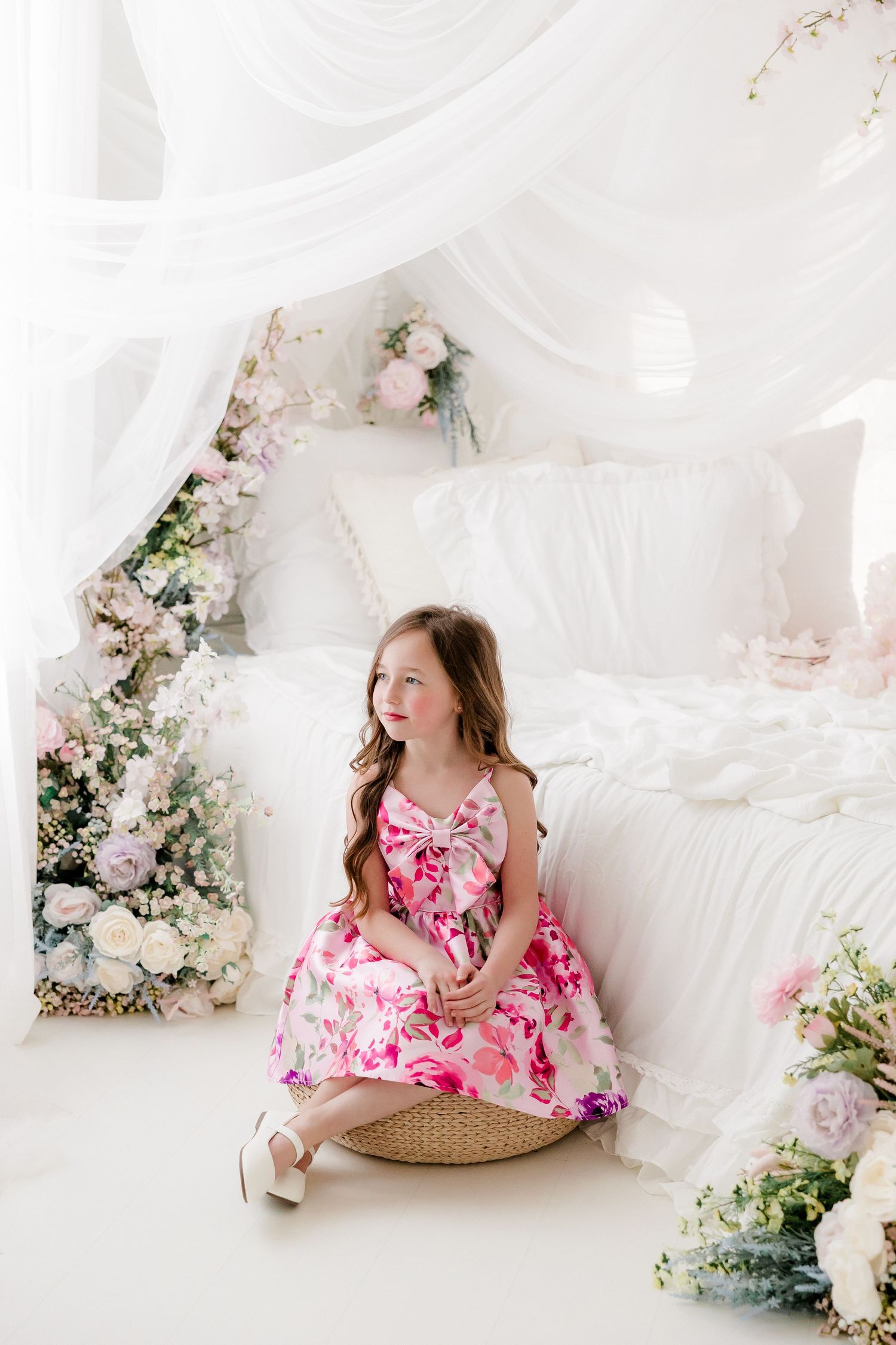 Dreamy white studio setting with floral arrangements and soft fabric draping creating an ethereal spring atmosphere.