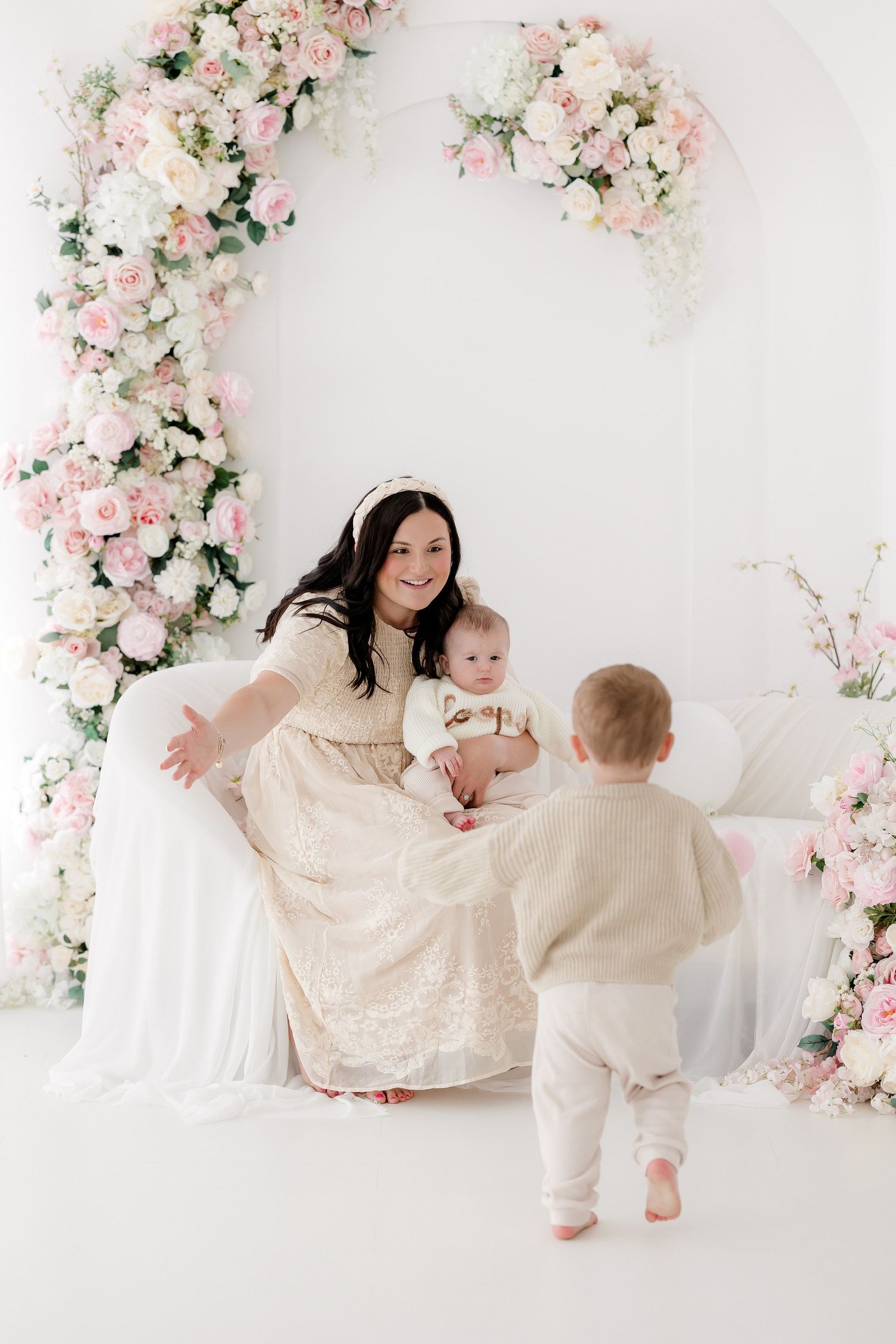 A floral photo session setup with pink and white roses against a white backdrop featuring mother and baby in matching outfits.
