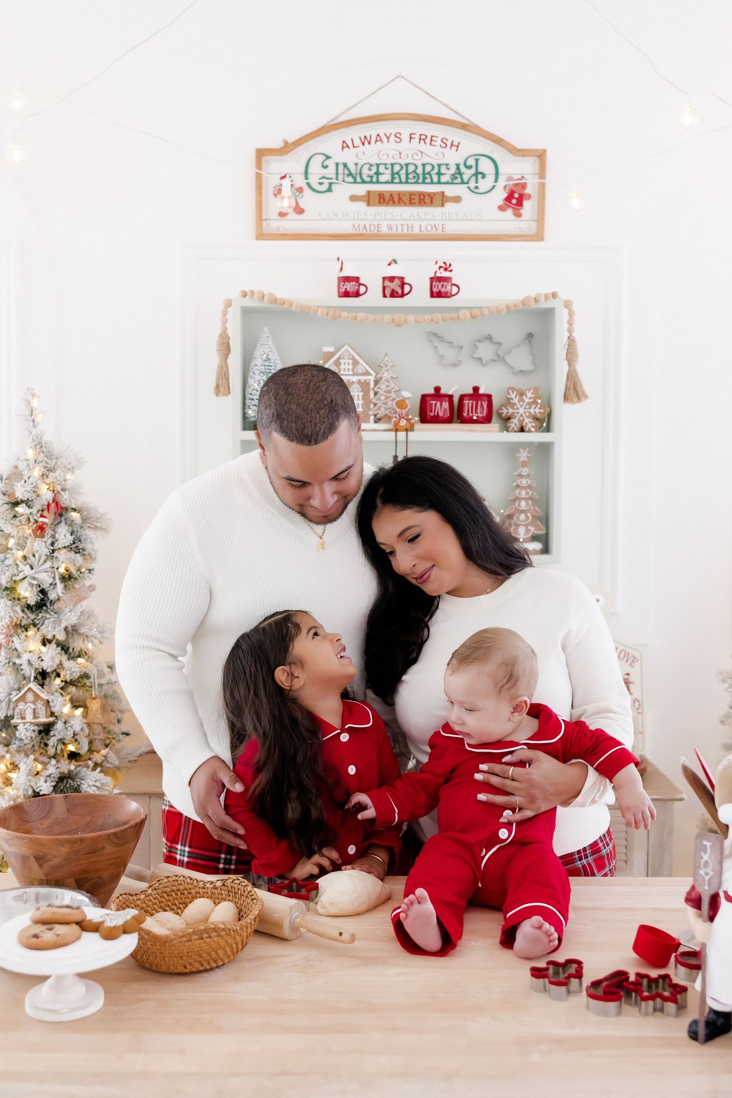 Family in matching red and white pajamas baking Christmas cookies together in a festive holiday kitchen.