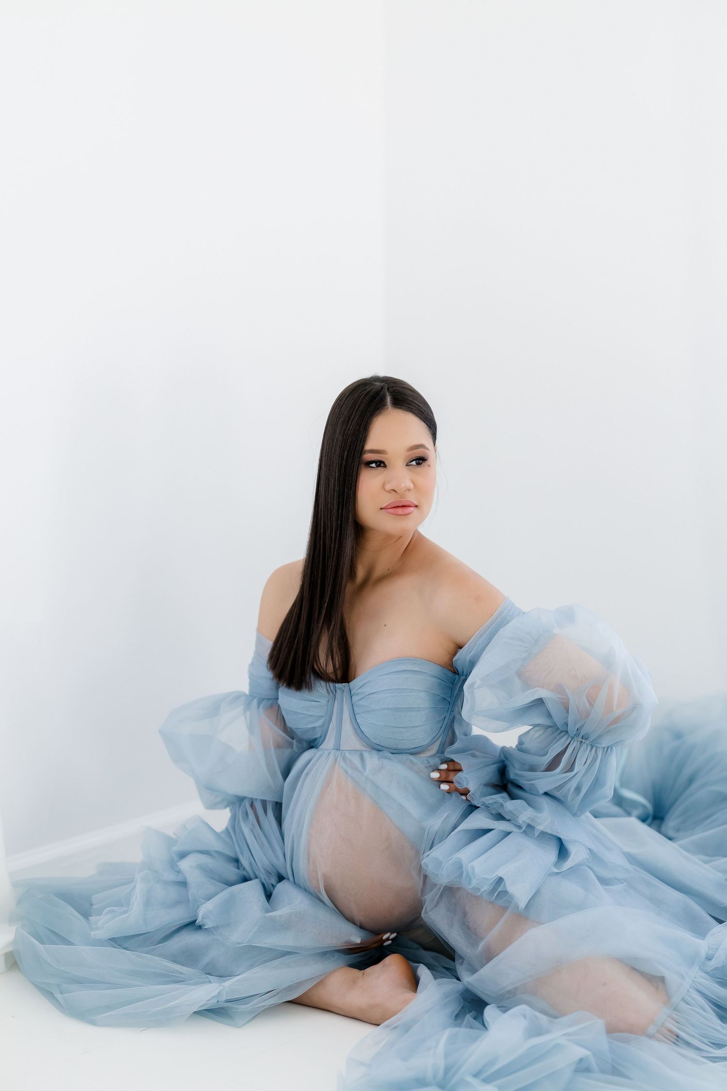 Artistic maternity poses in a light blue sheer dress on white background.