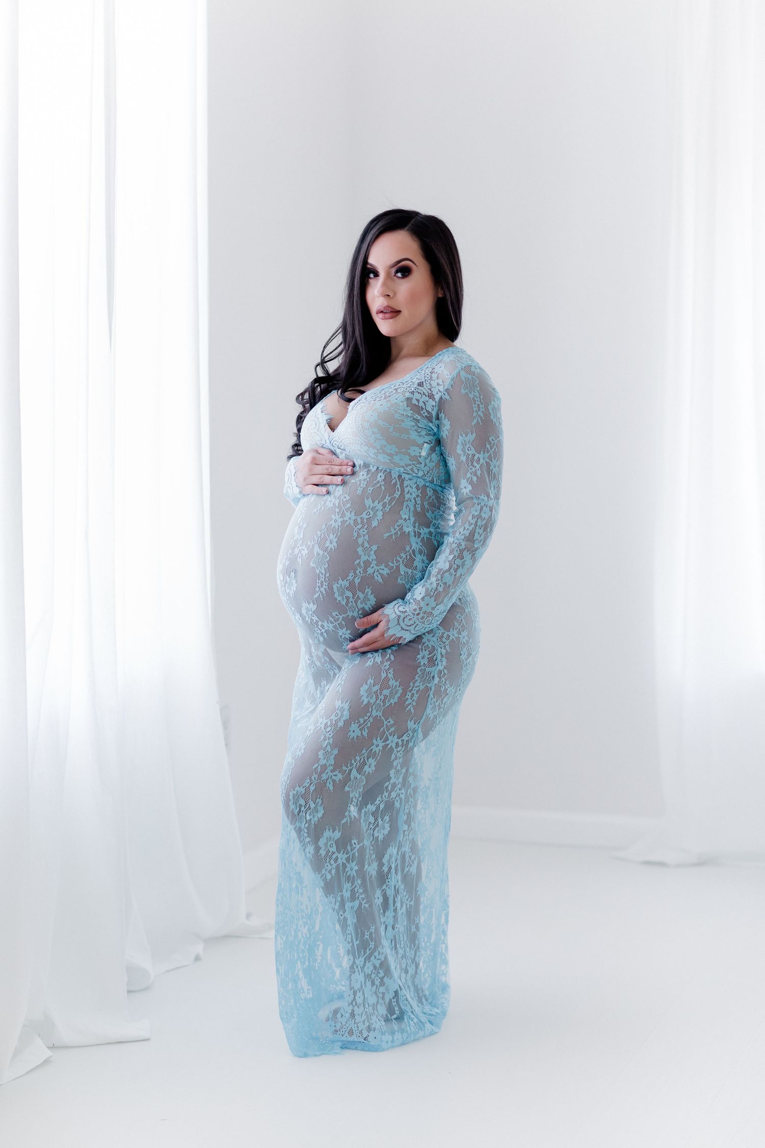 Light blue lace maternity gown showcased in elegant studio portrait against white background.