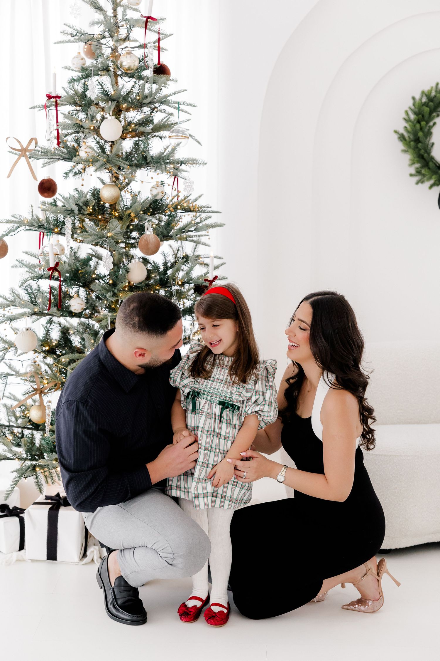 Family sharing joyful moment together by decorated Christmas tree in white studio setting.