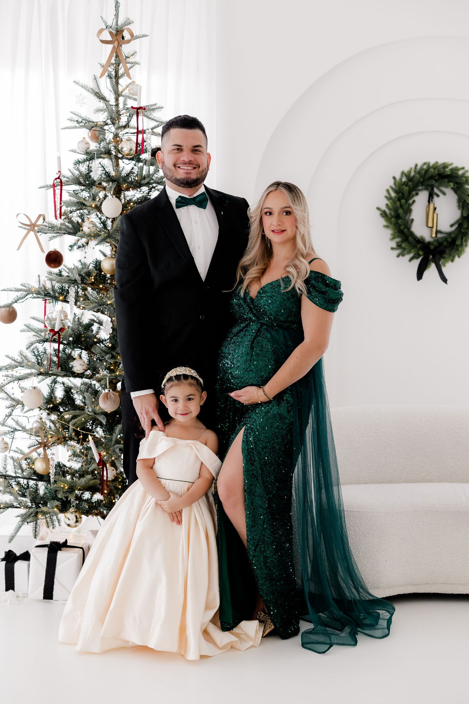 Holiday family portrait with three people in formal attire posed in front of a decorated Christmas tree.