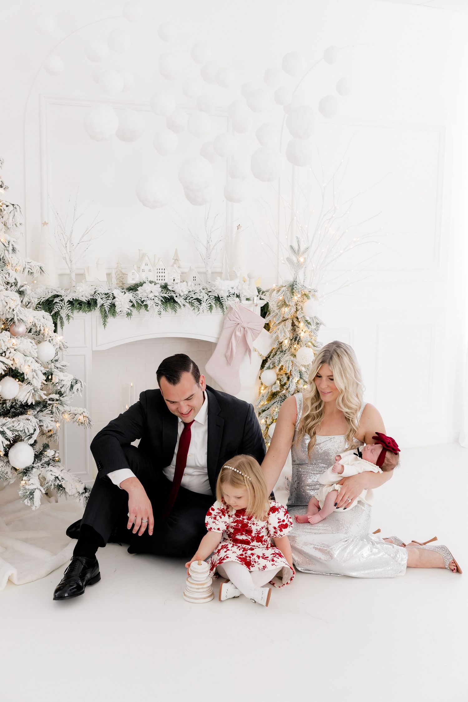 Holiday photo session in white studio with Christmas trees and floral decorations.