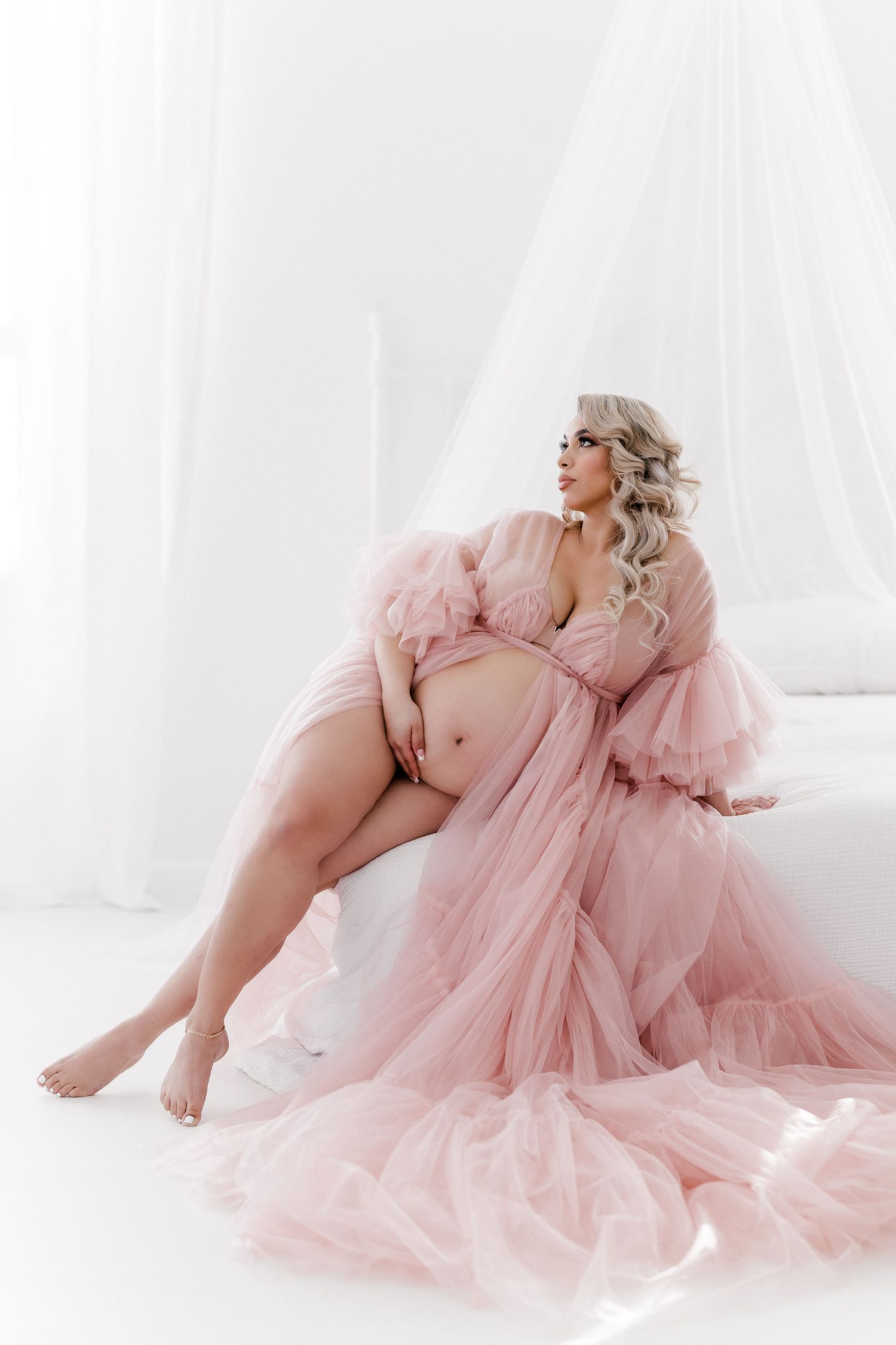 Ethereal maternity photos featuring flowy pink tulle gown in bright white studio setting.