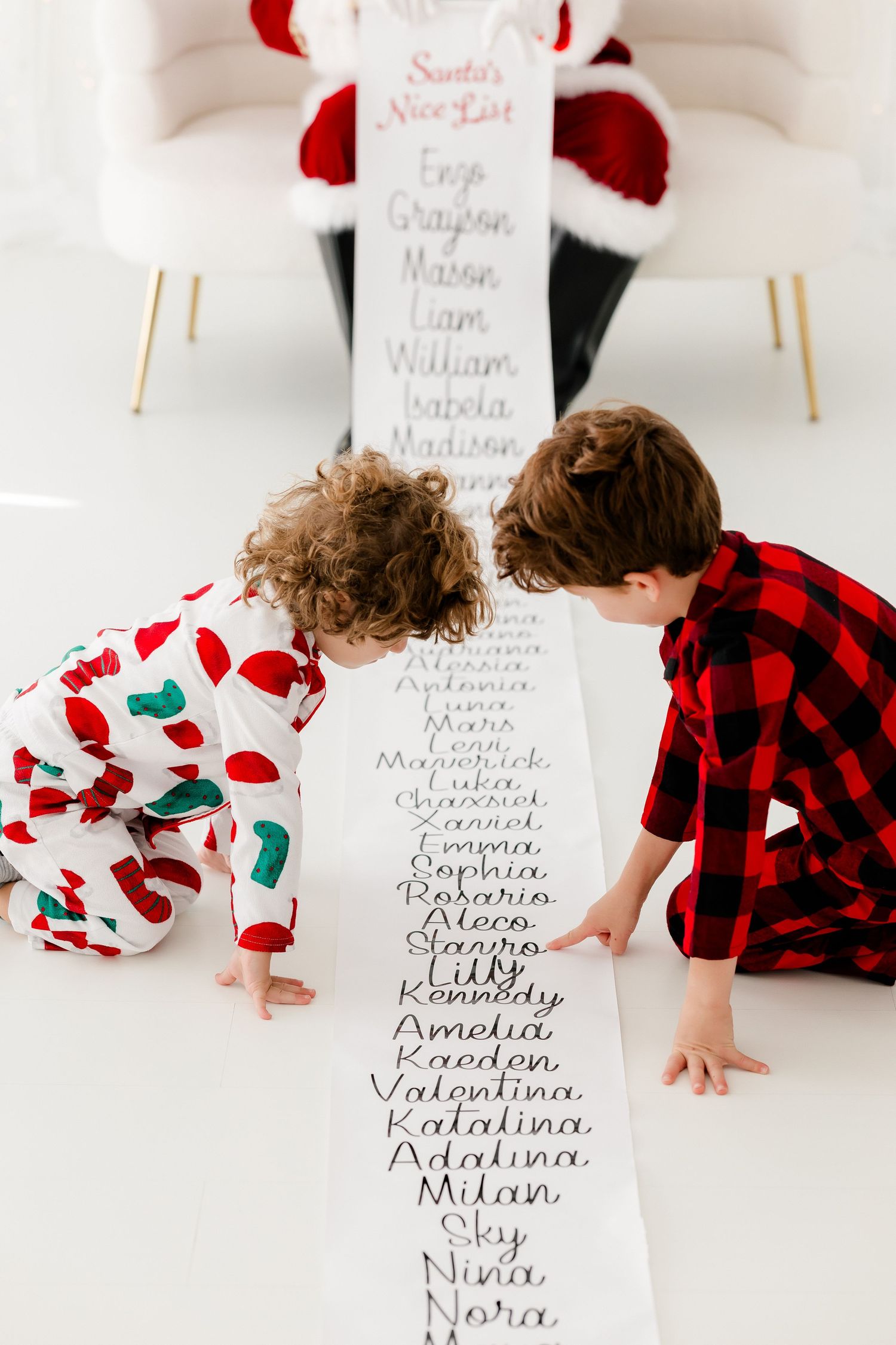 Two children in Christmas pajamas reading Santa's Nice List scroll on the floor.