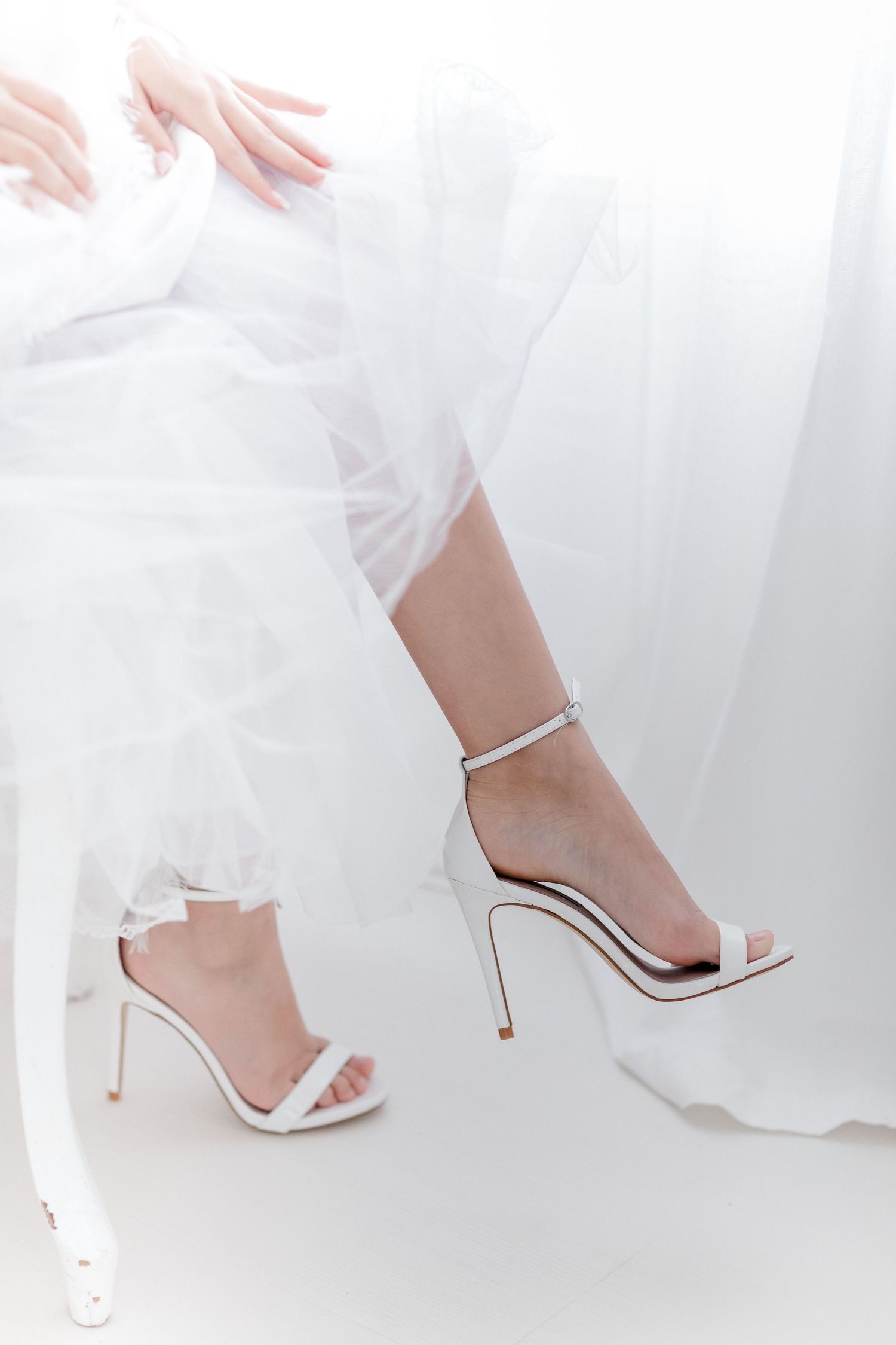 Close-up view of elegant white bridal shoes with delicate straps and high heels against a light background.