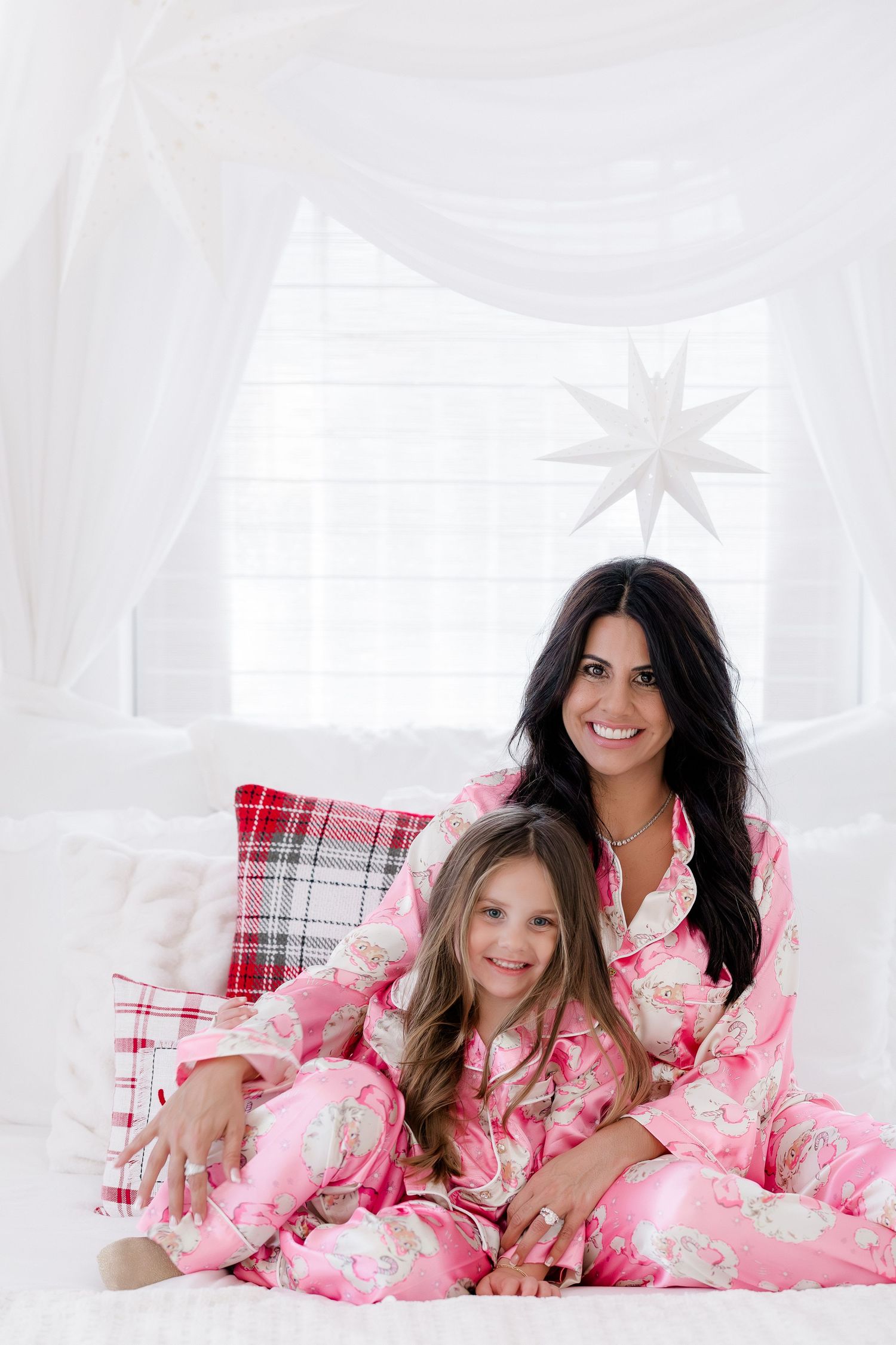 Mother and daughter wearing matching pink floral pajamas sitting together on a white bed with holiday decorations.