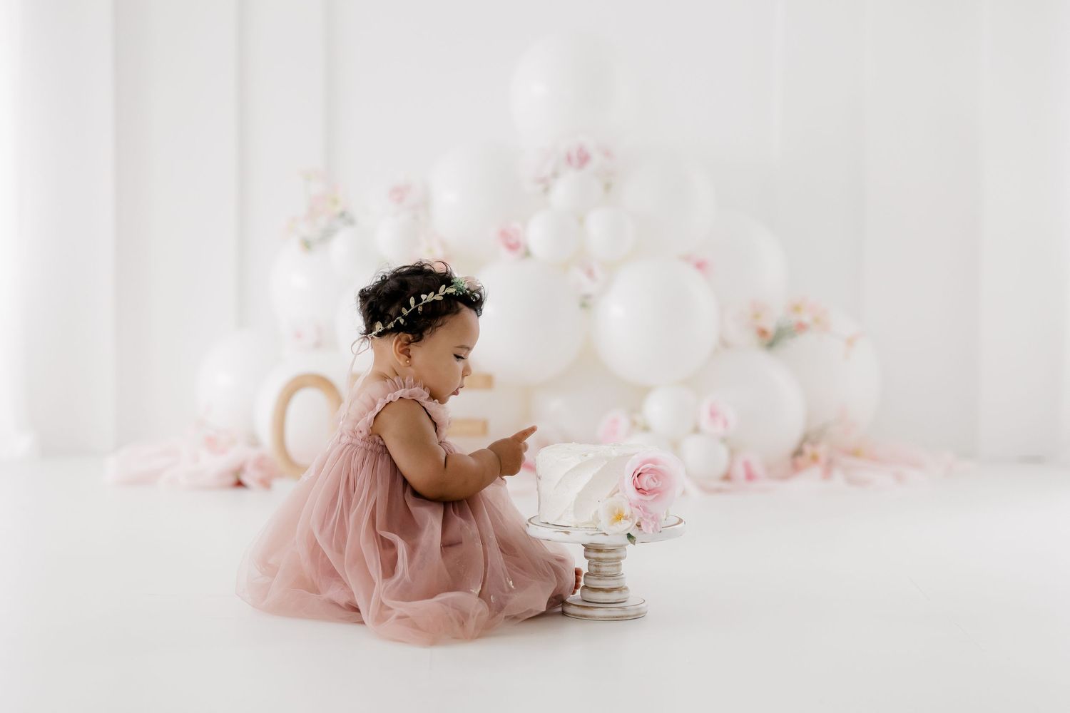 Soft pink and white party setup with balloons and floral arrangements in a minimalist studio setting.