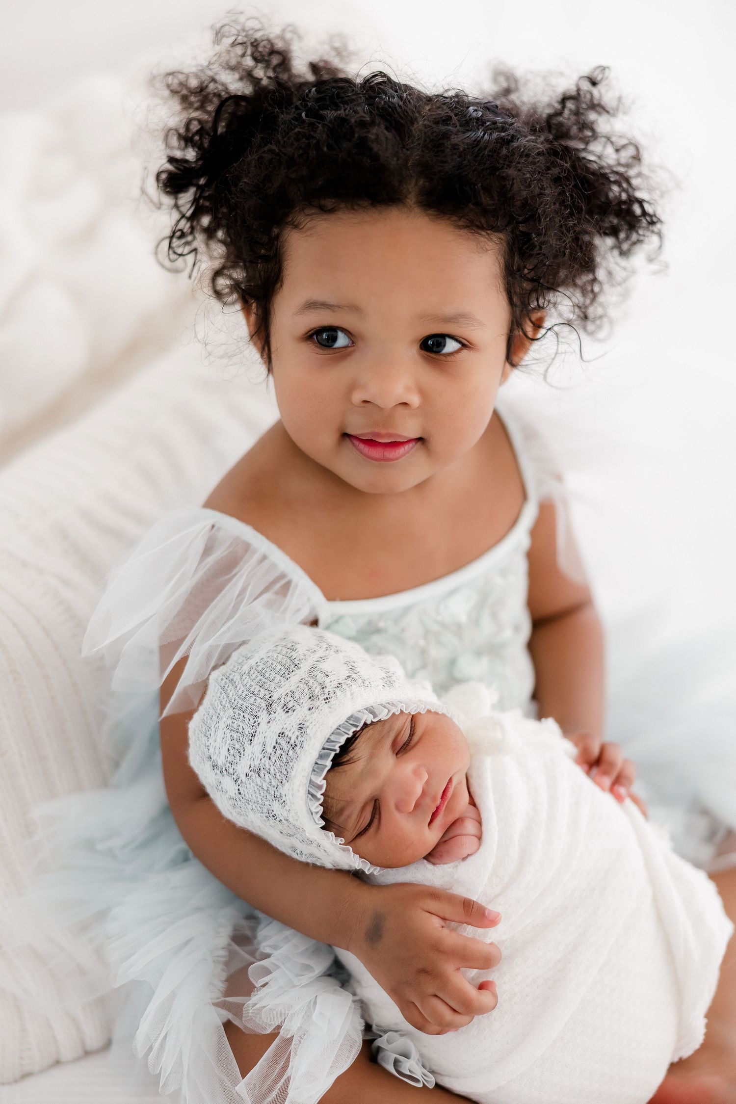 A sweet sibling moment in white lace outfits against a light backdrop.