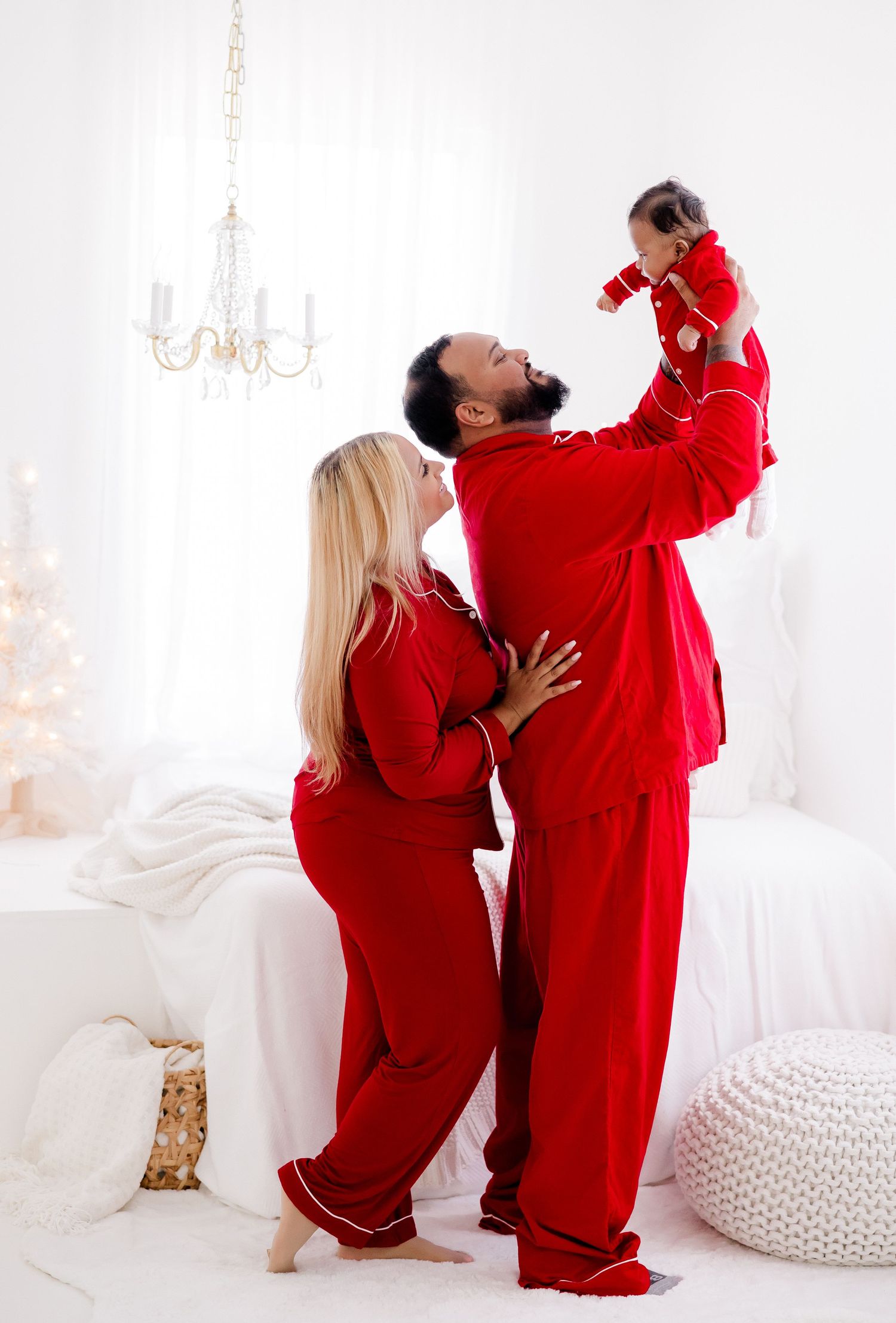 Family wearing matching red pajamas playing and laughing together in white studio setting.