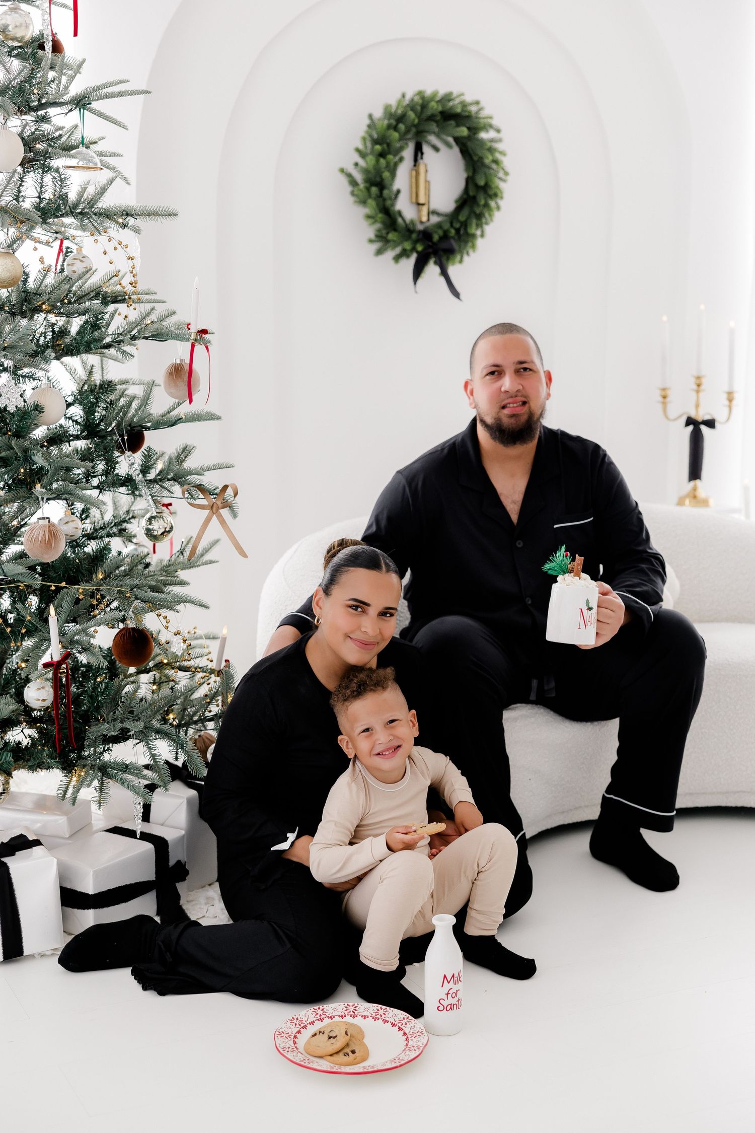 Family holiday photoshoot with matching black pajamas next to decorated Christmas tree.