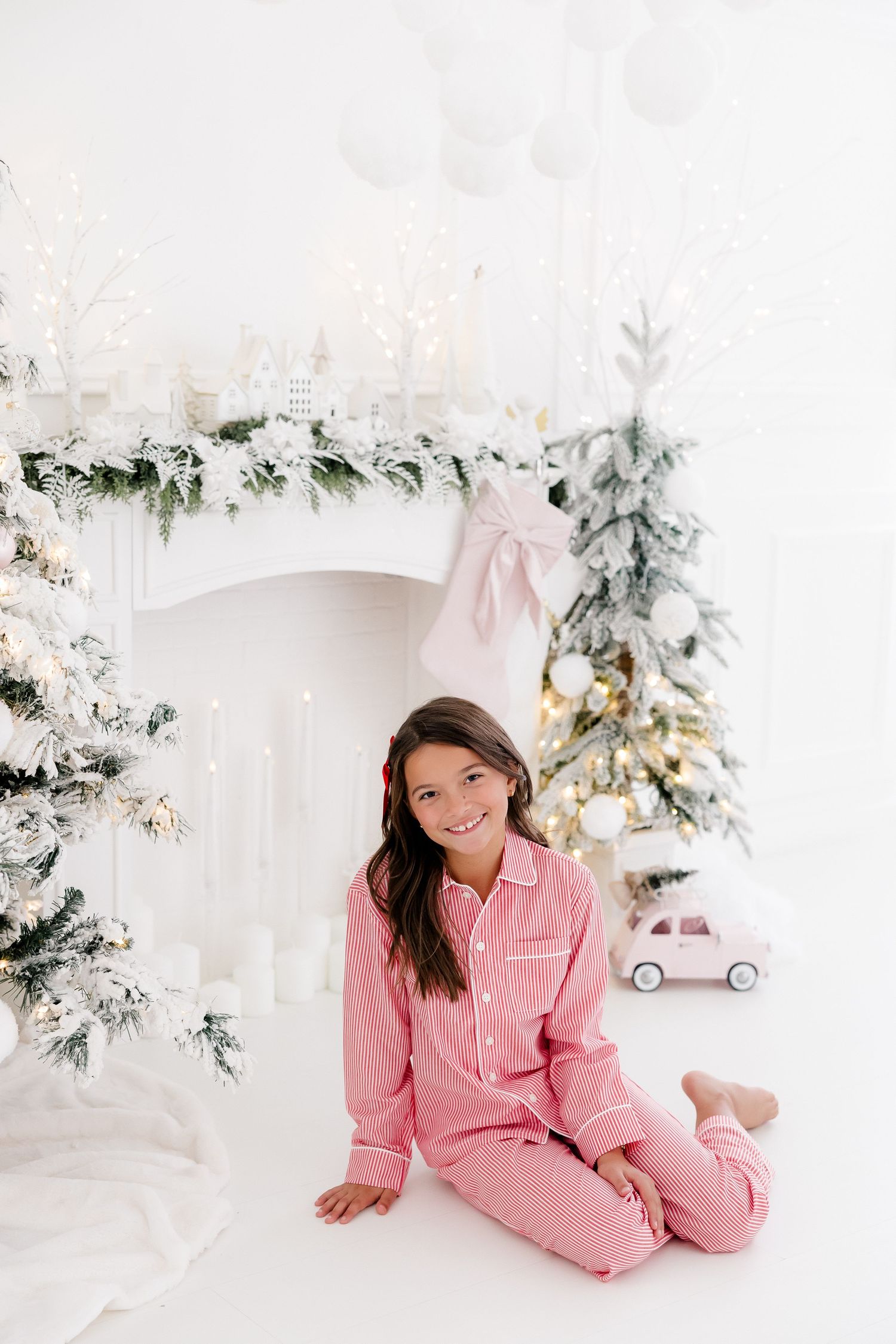Holiday portraits in pink pajamas with white Christmas trees and vintage toy car props.
