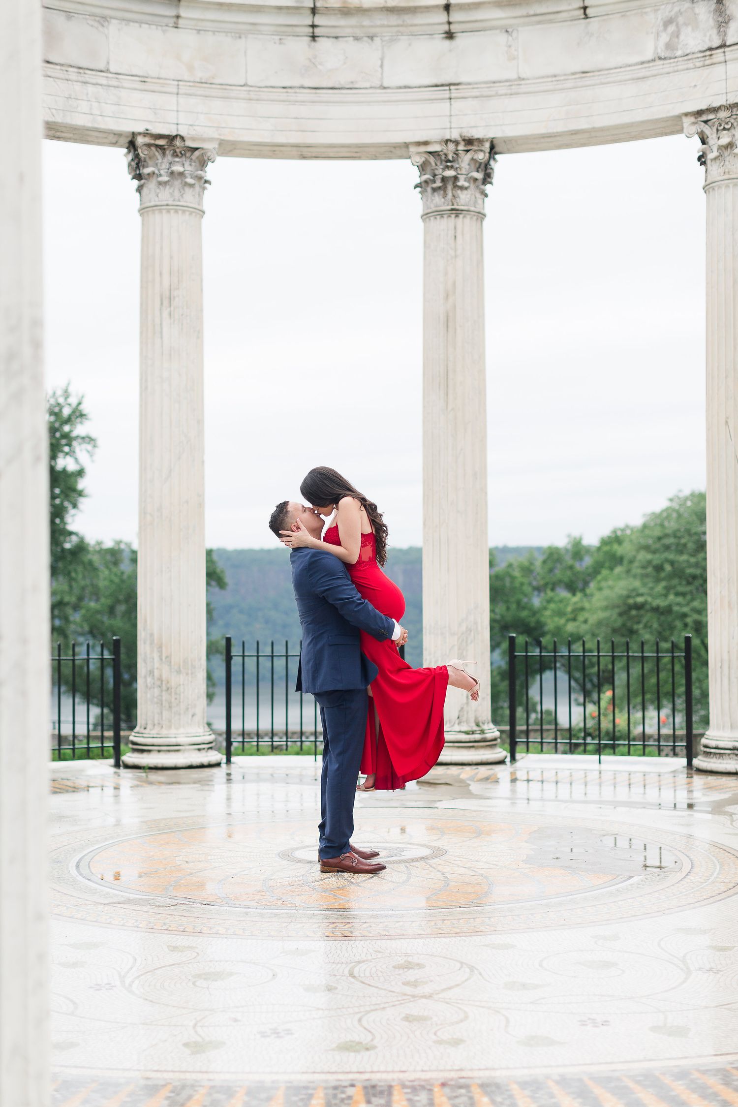 A romantic couple embraces in a dip pose under an elegant white columned rotunda during a photo session.