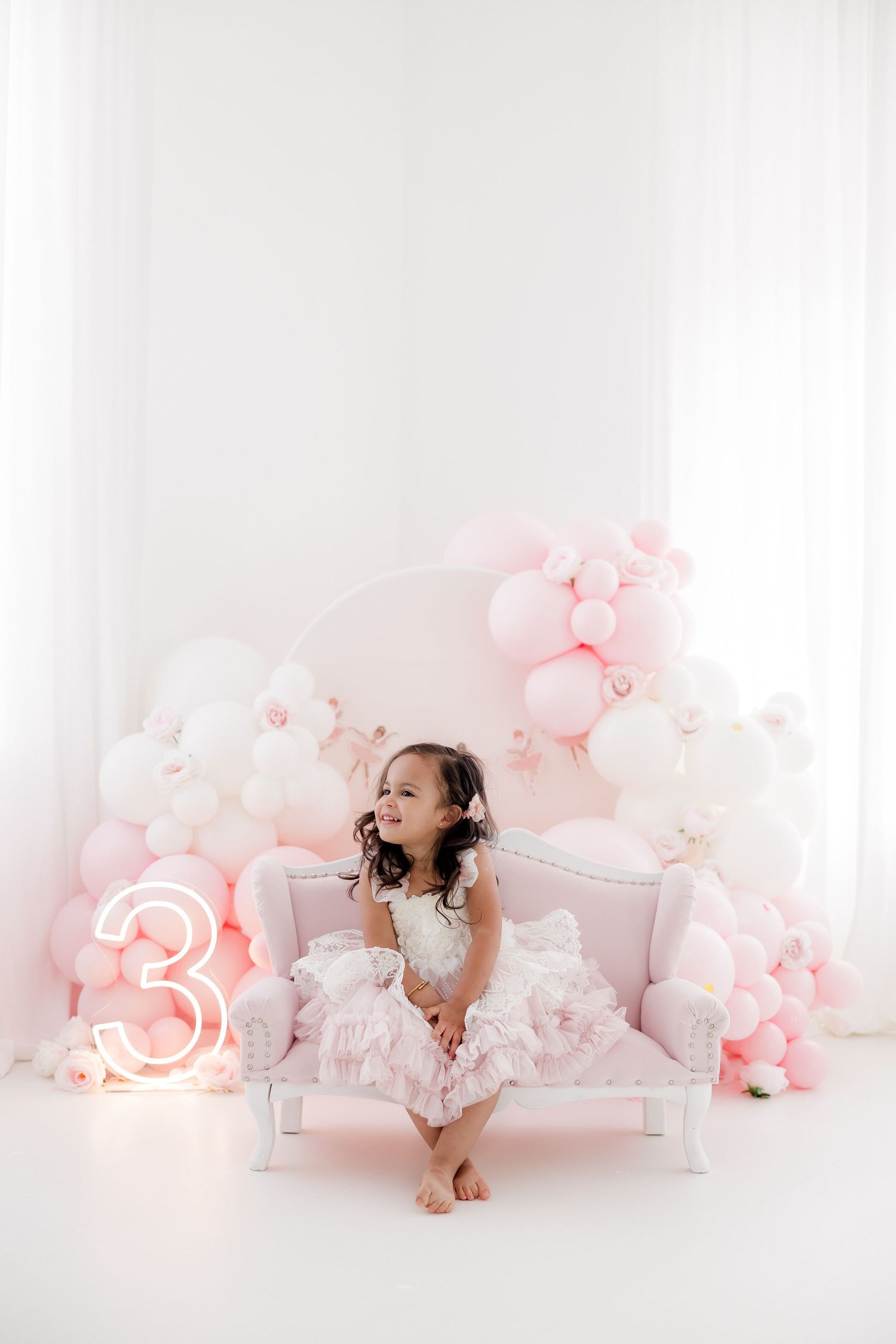 Dreamy pink and white photo session setup with balloons, flowers, and delicate decor creating a soft ethereal atmosphere.