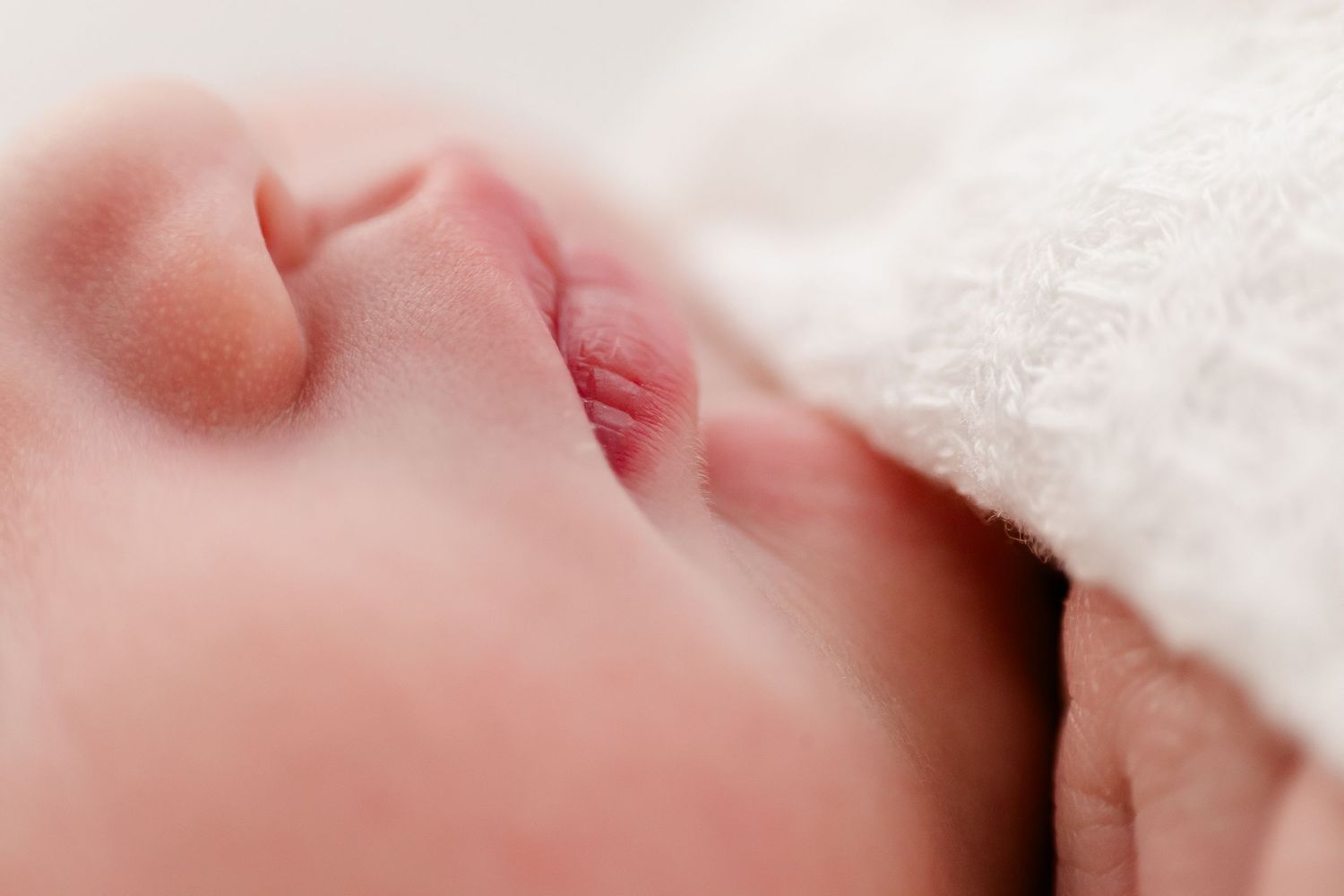 Close-up view of a sleeping baby's face partially covered with a soft white blanket.