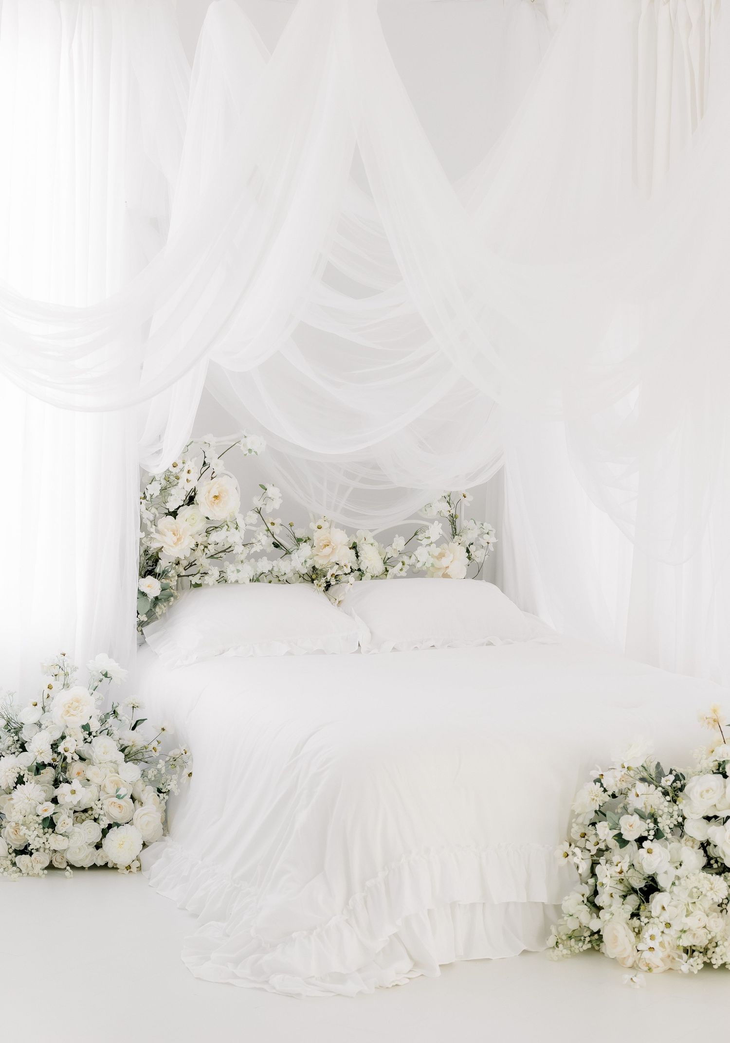Elegant white floral backdrop with draped fabric and white rose arrangements for a romantic wedding setting.