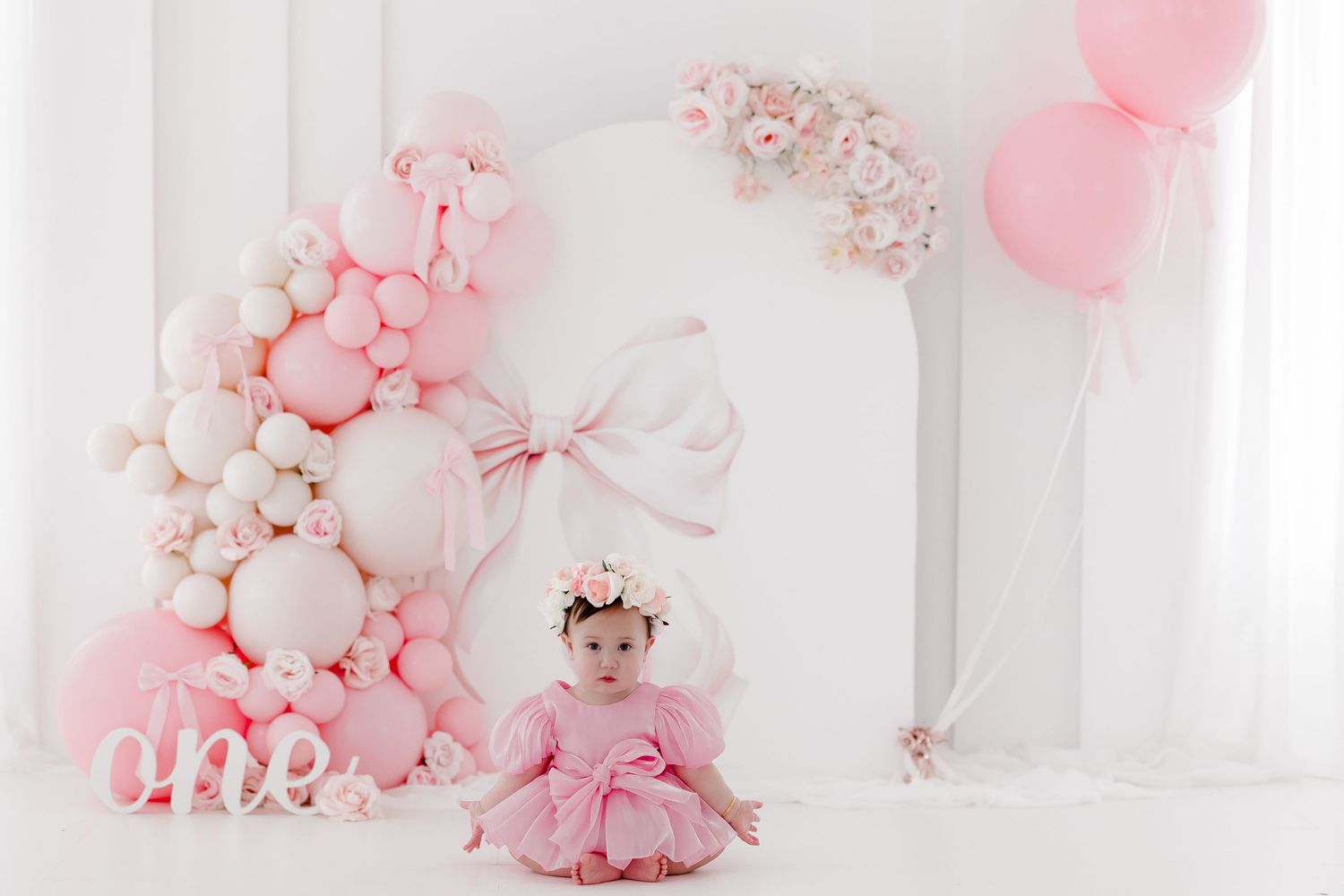 Pink and white balloon decorations create an elegant party setup with soft lighting and delicate floral accents.