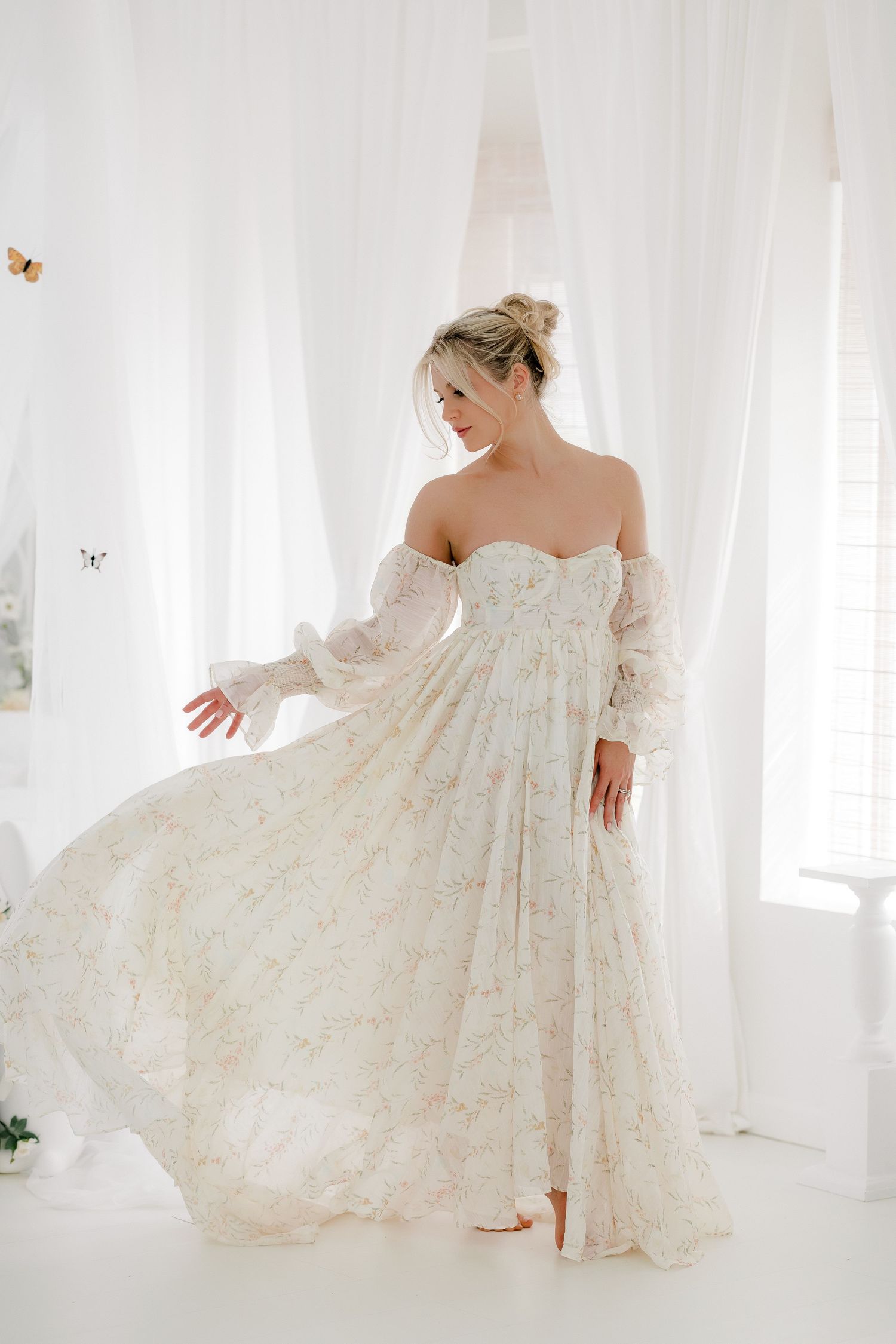 A flowing off-shoulder lace wedding gown twirls gracefully in a bright white studio setting.
