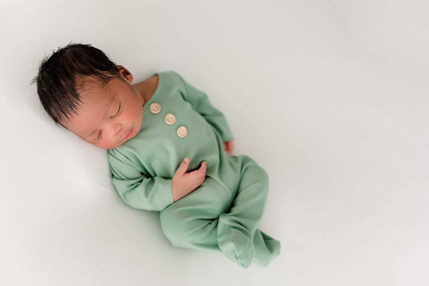 Sleeping newborn wearing mint green buttoned outfit against white background.