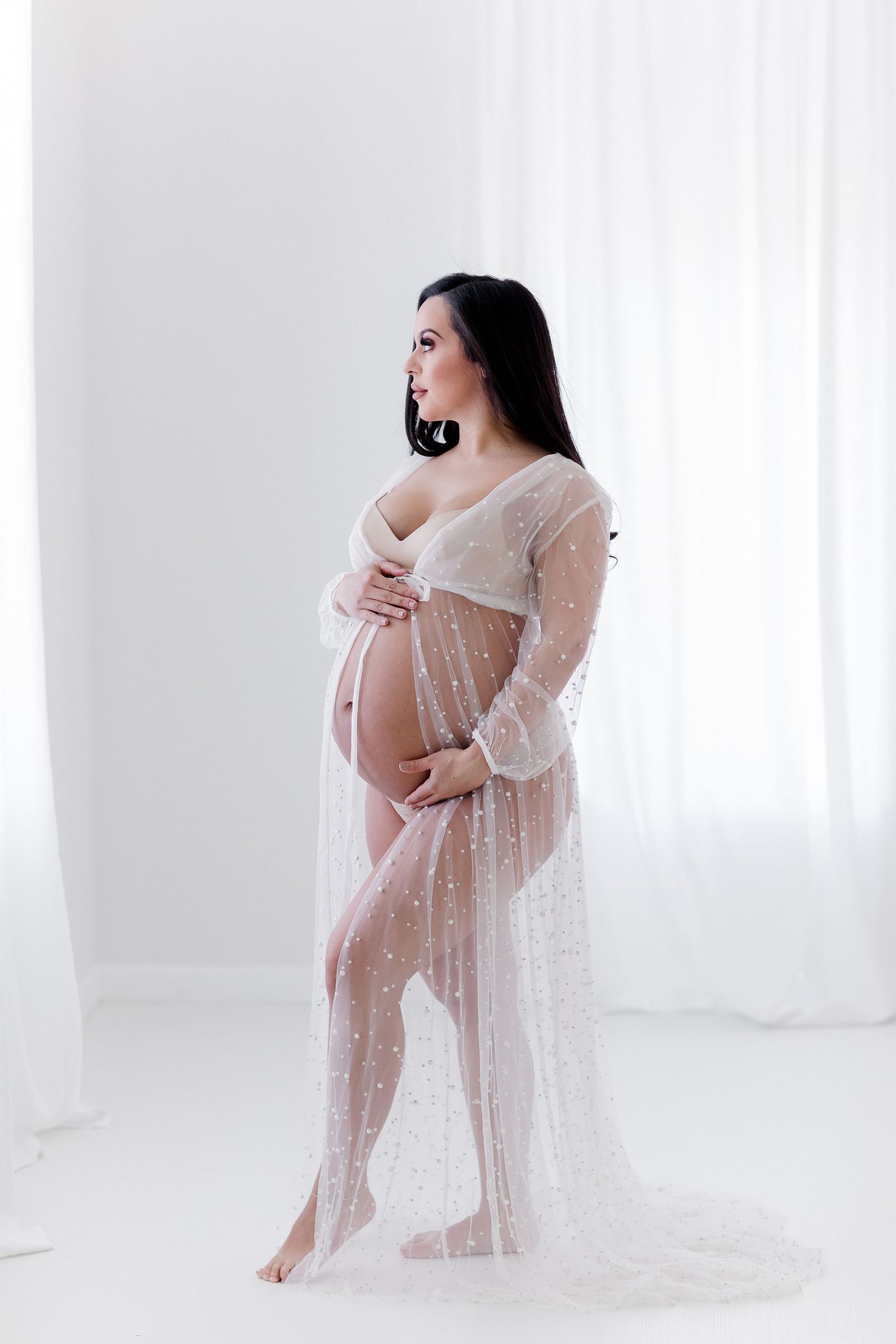 Soft and romantic maternity portrait with sheer lace overlay in bright studio setting.