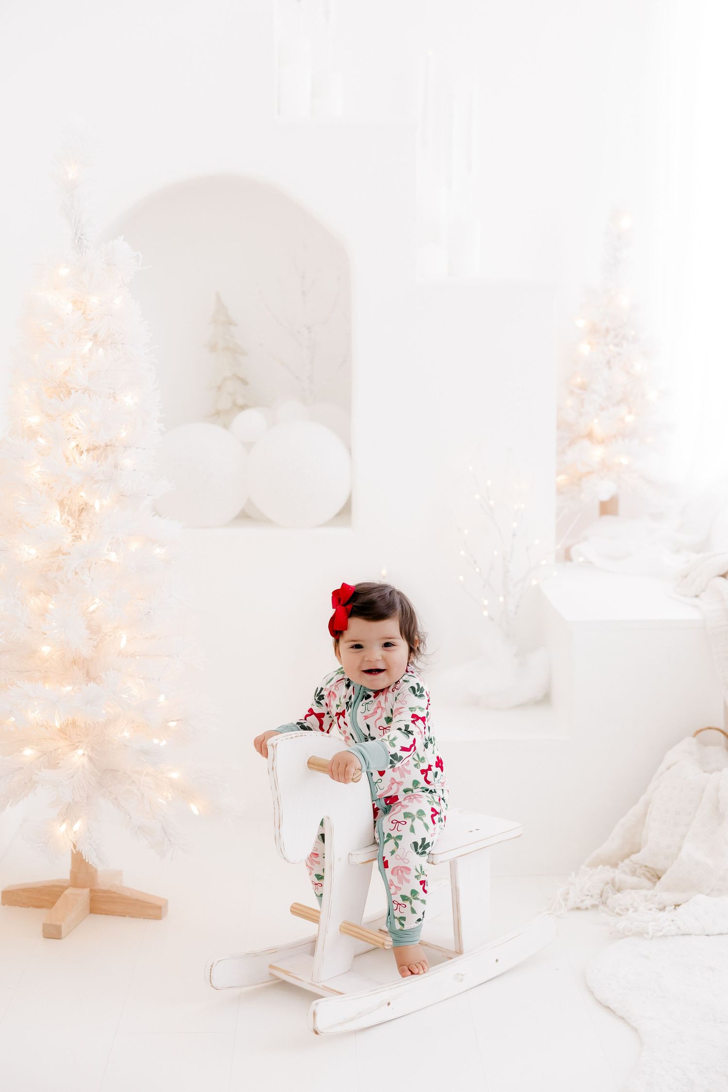Child in festive outfit playing on white rocking horse with Christmas decorations.