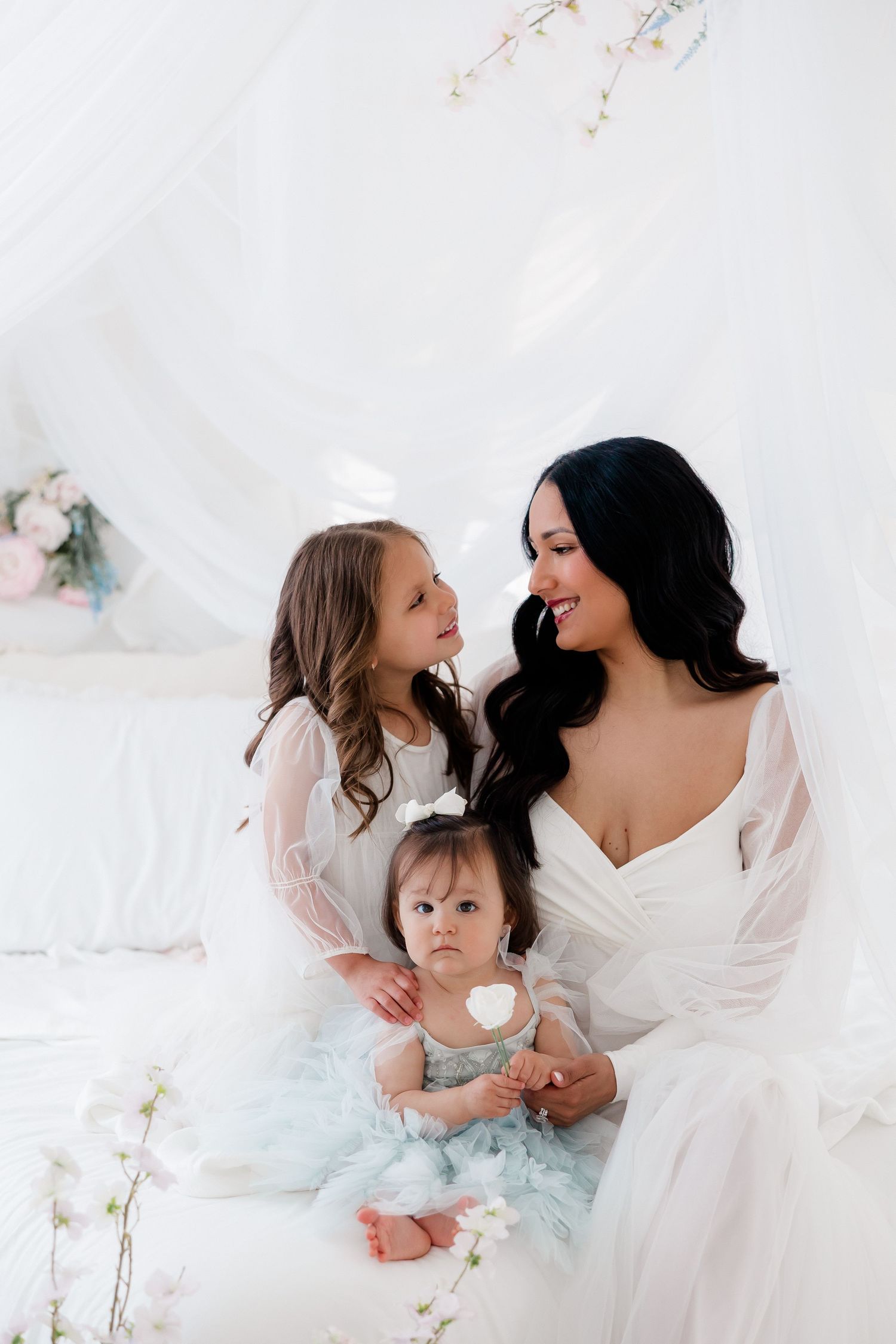 A tender moment captured in a dreamy white setting with a mother and children sharing joyful expressions.