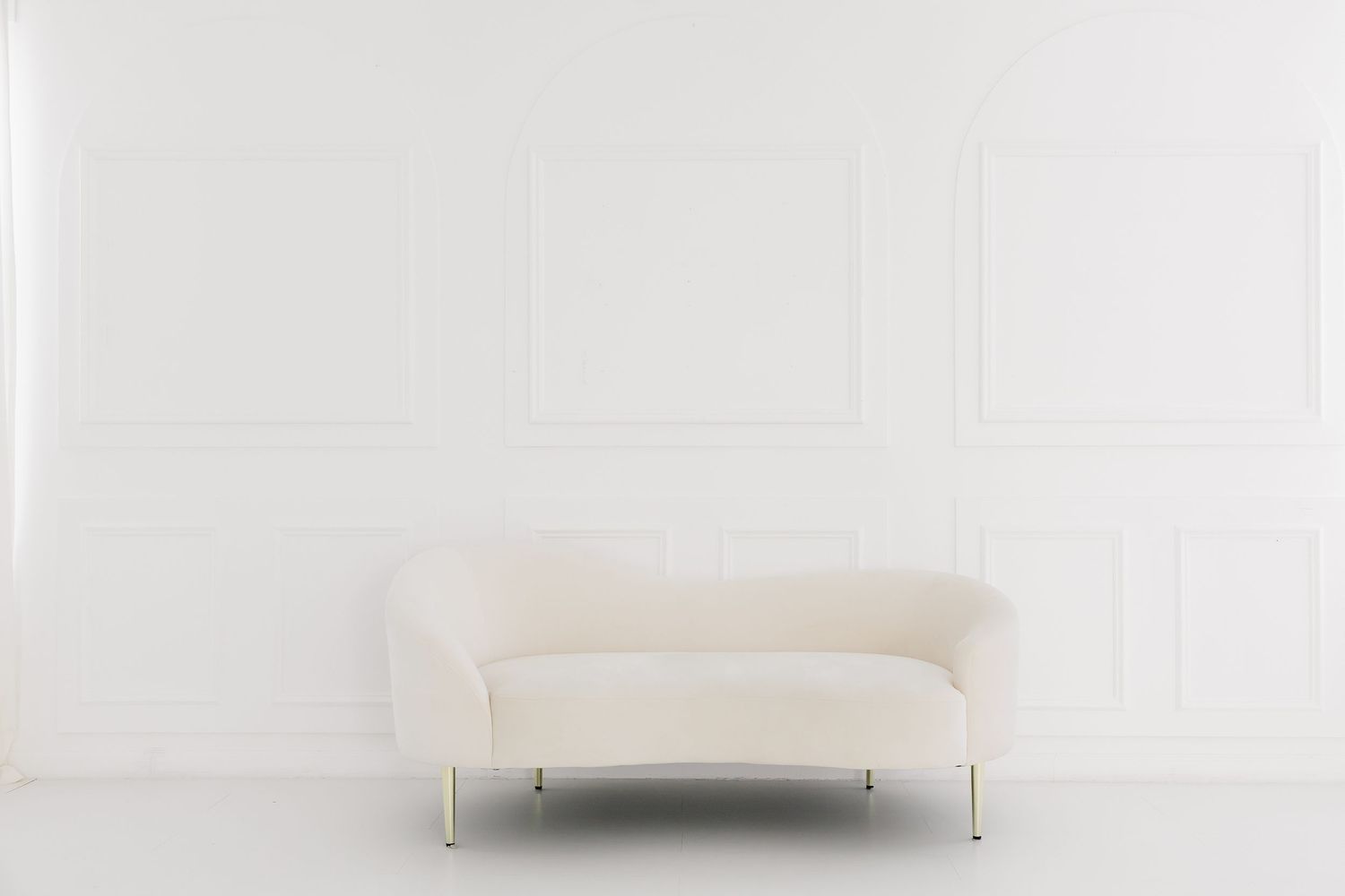 Modern white sofa with clean lines and slim metal legs sits elegantly against a white wall.
